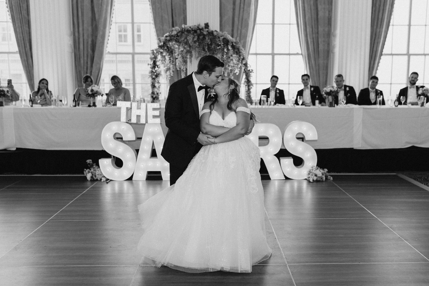 Bride and groom share first dance before illuminated THE SAUERS marquee letters at reception.