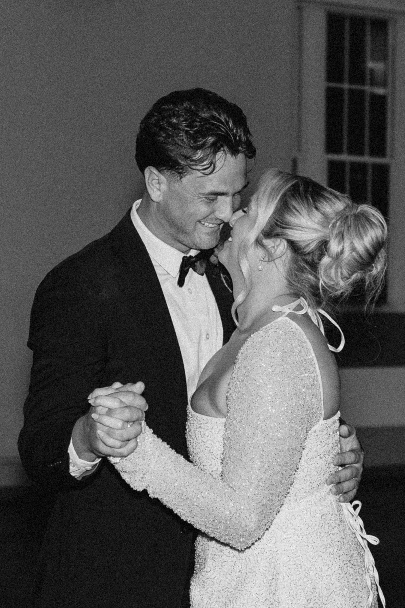 Black and white photo of bride and groom sharing first dance outdoors at night.