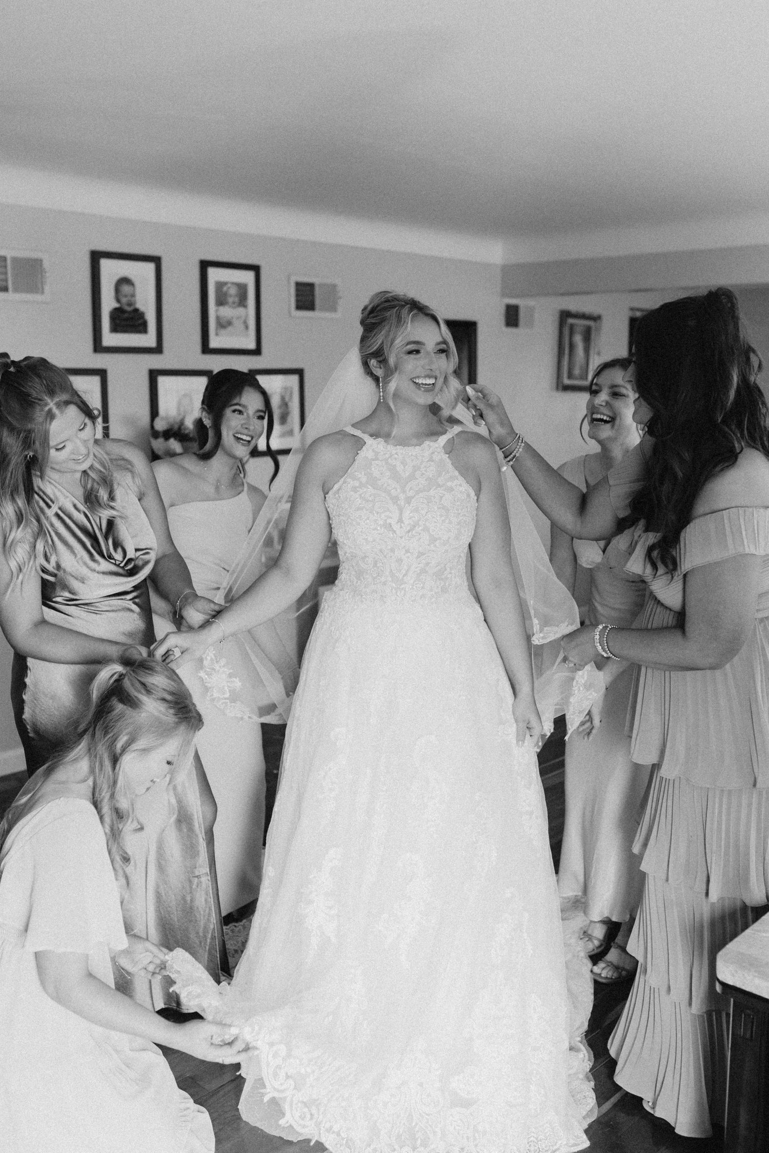 Bride in lace wedding dress laughing as bridesmaids help her get ready before the ceremony.