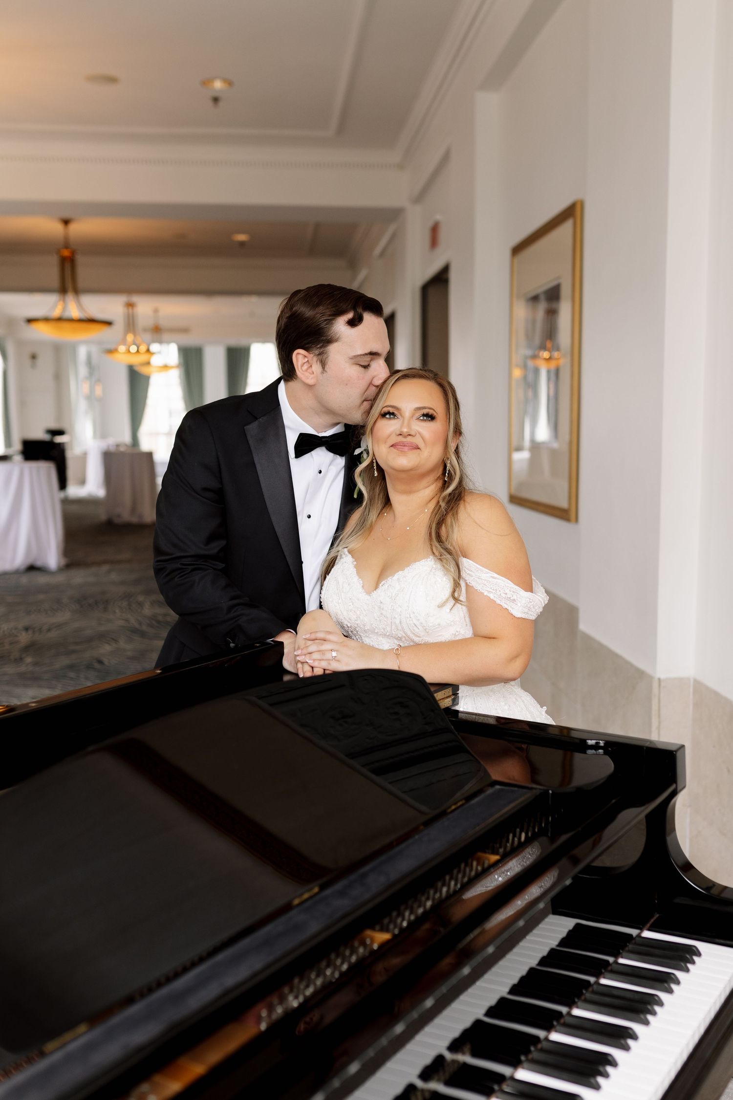 Bride and groom sharing a romantic moment at a grand piano in an elegant ballroom.
