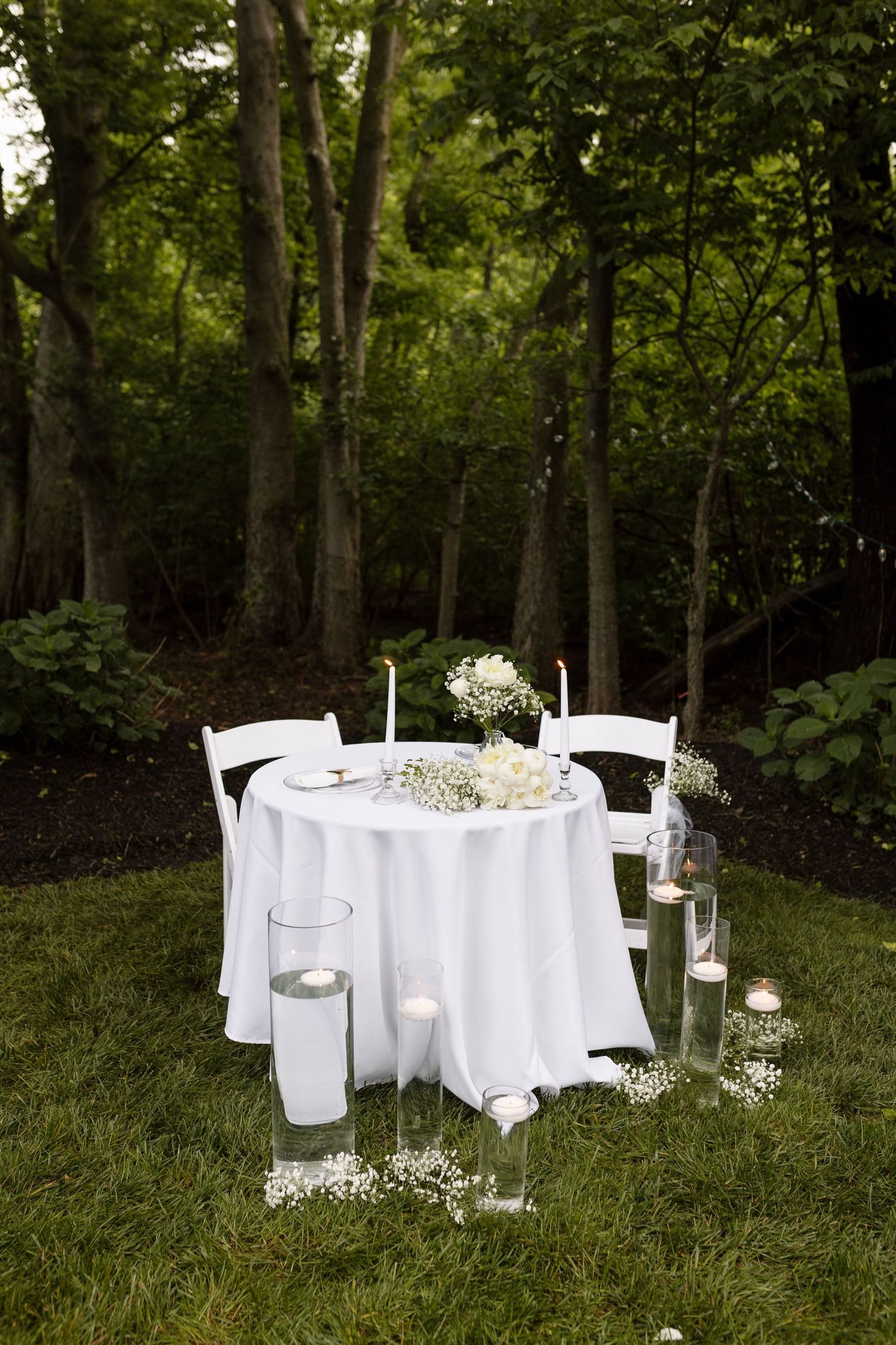 Elegant outdoor wedding table with white linens, floral centerpiece, candles, and floating votives.