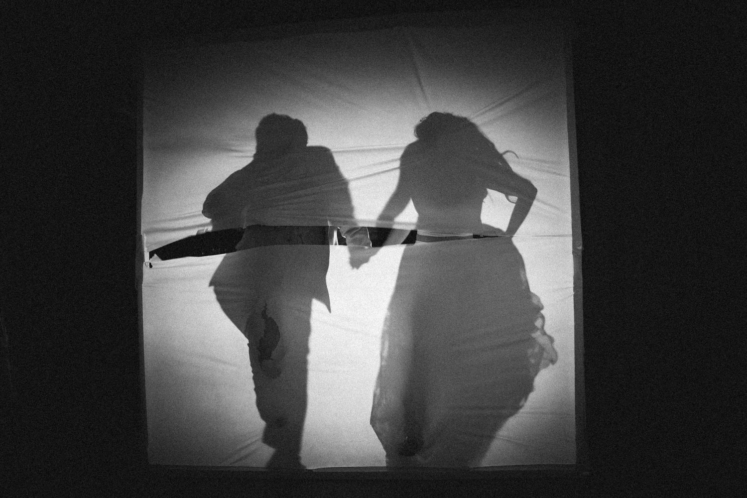Dramatic black and white silhouette of bride and groom dancing behind tent wall.