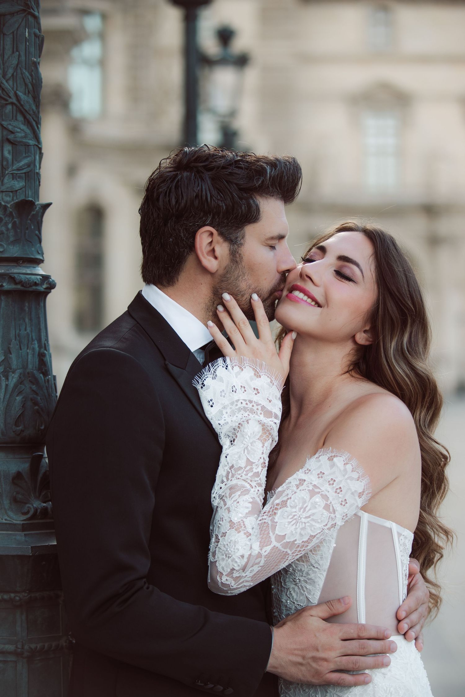 Bride and groom share a romantic kiss near a vintage lamppost in Paris, bride wearing lace off-shoulder wedding gown.