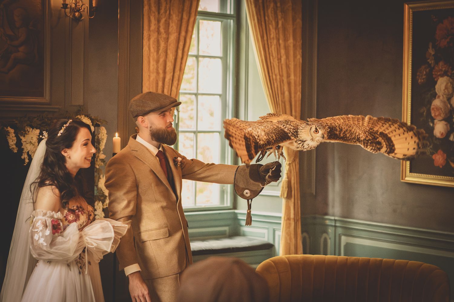 Bride and groom holding an owl on a gloved hand in an elegant vintage manor house interior.