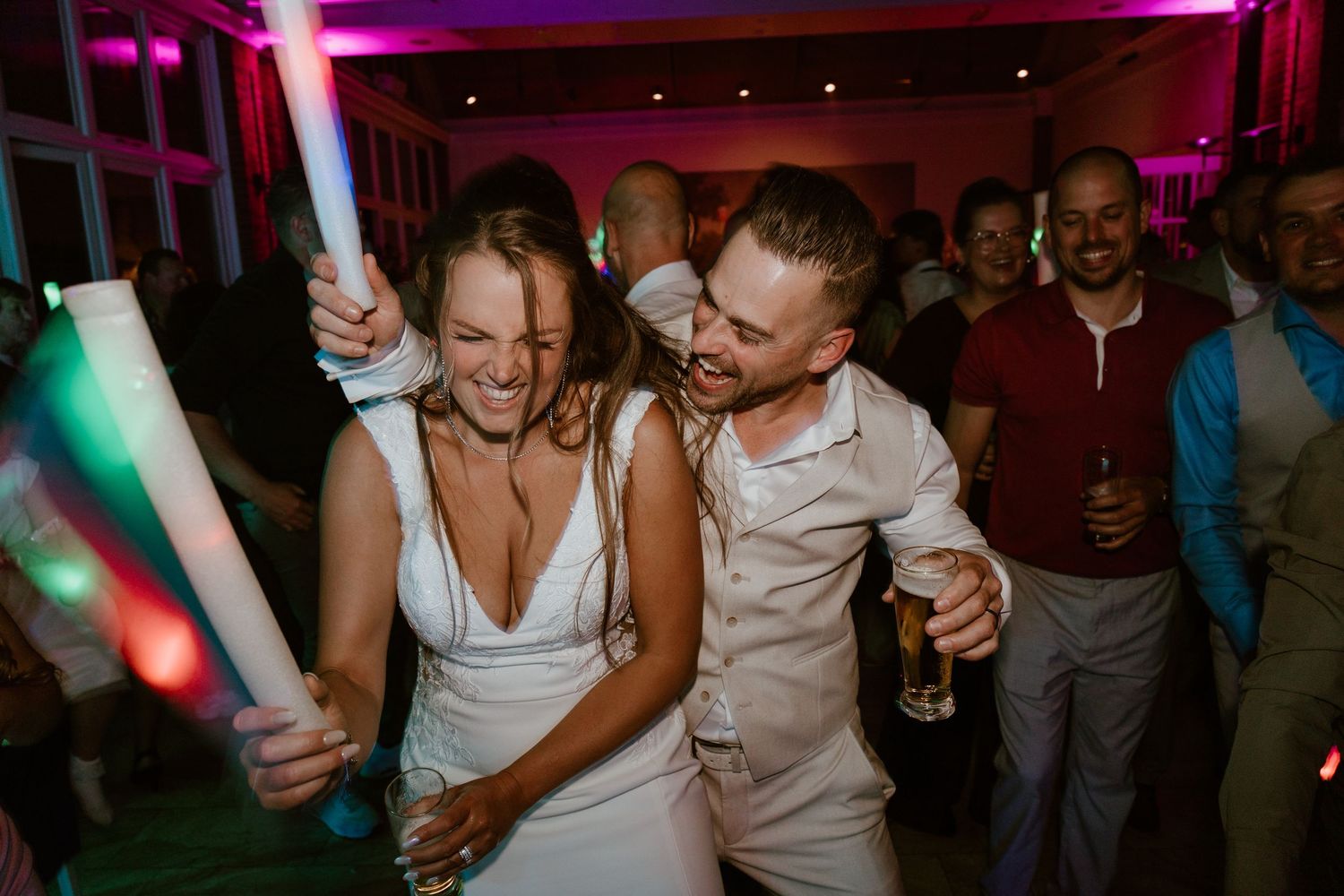 Bride and groom celebrate joyfully with glow sticks on the wedding reception dance floor.