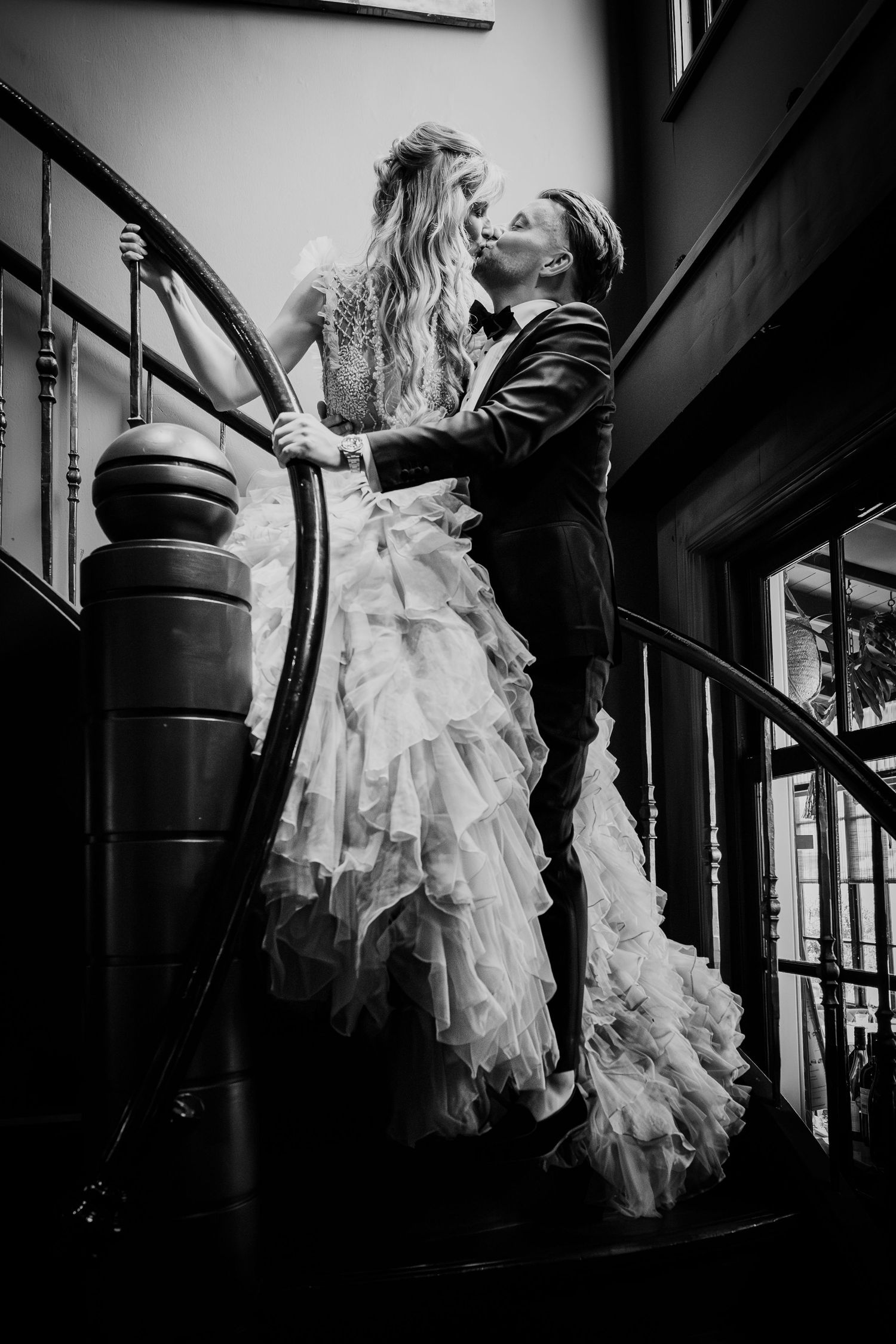 Black and white photo of bride and groom sharing a romantic kiss on a spiral staircase.
