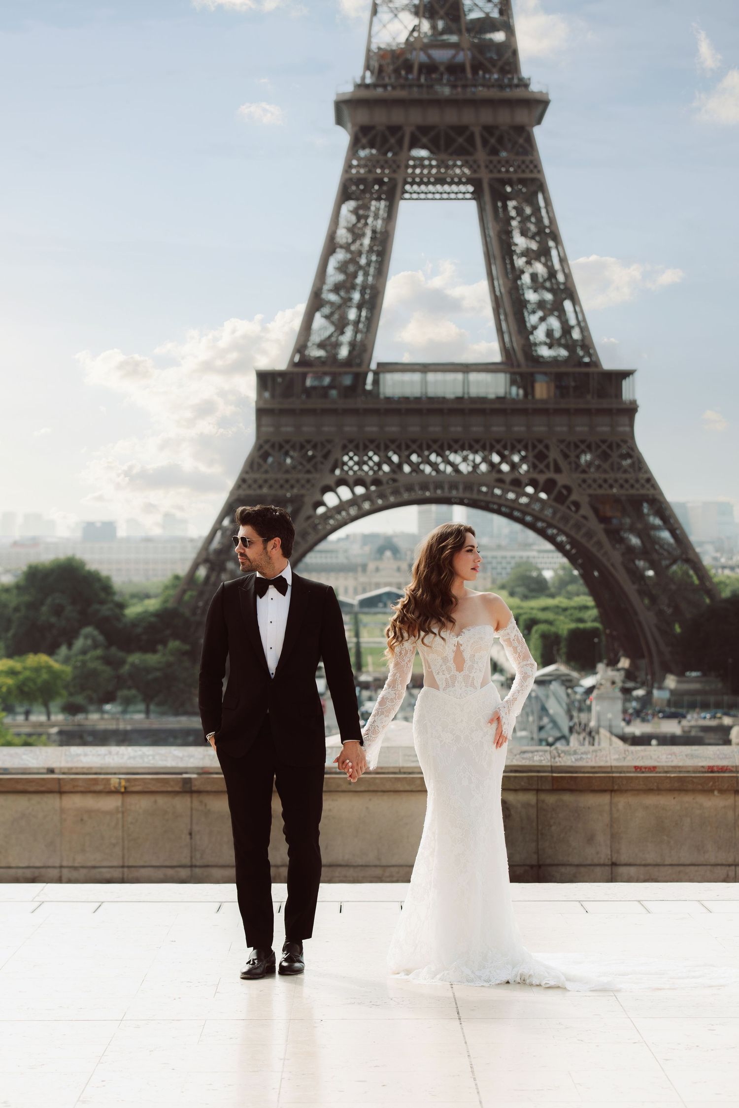 Bride and groom hold hands before the iconic Eiffel Tower in Paris on their wedding day.