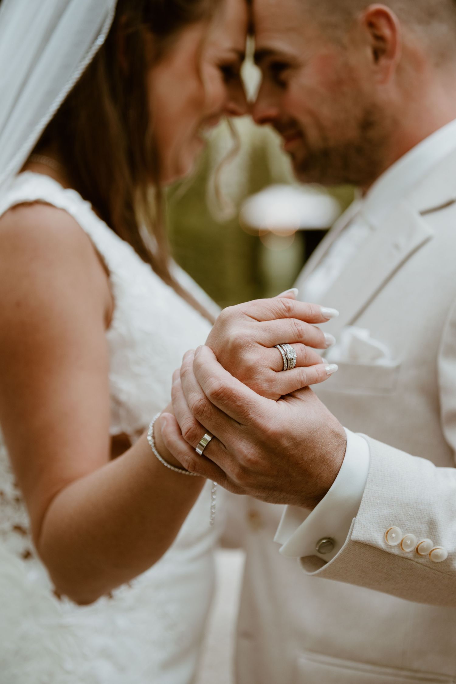 Close-up of bride and groom holding hands showing wedding rings during romantic moment.