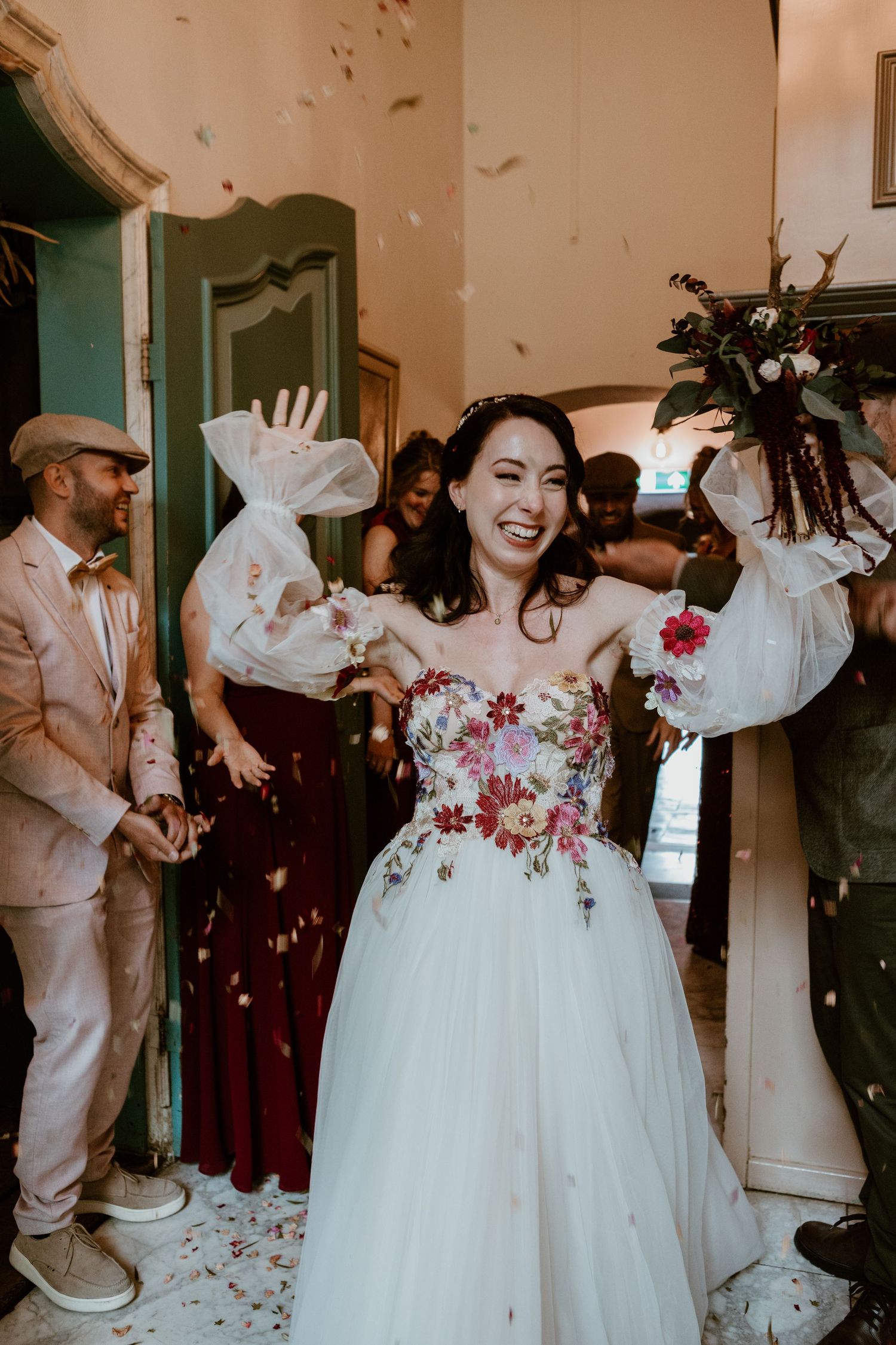 Joyful bride in floral embroidered gown celebrates with confetti shower at wedding exit.