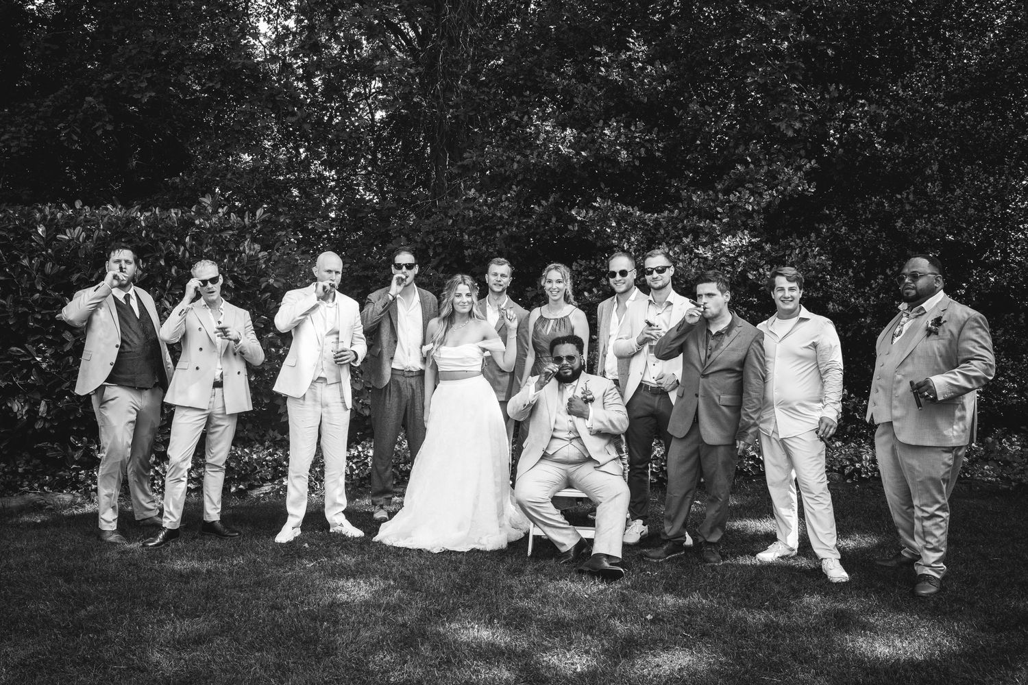 Black and white wedding party group photo with sunglasses on green lawn.