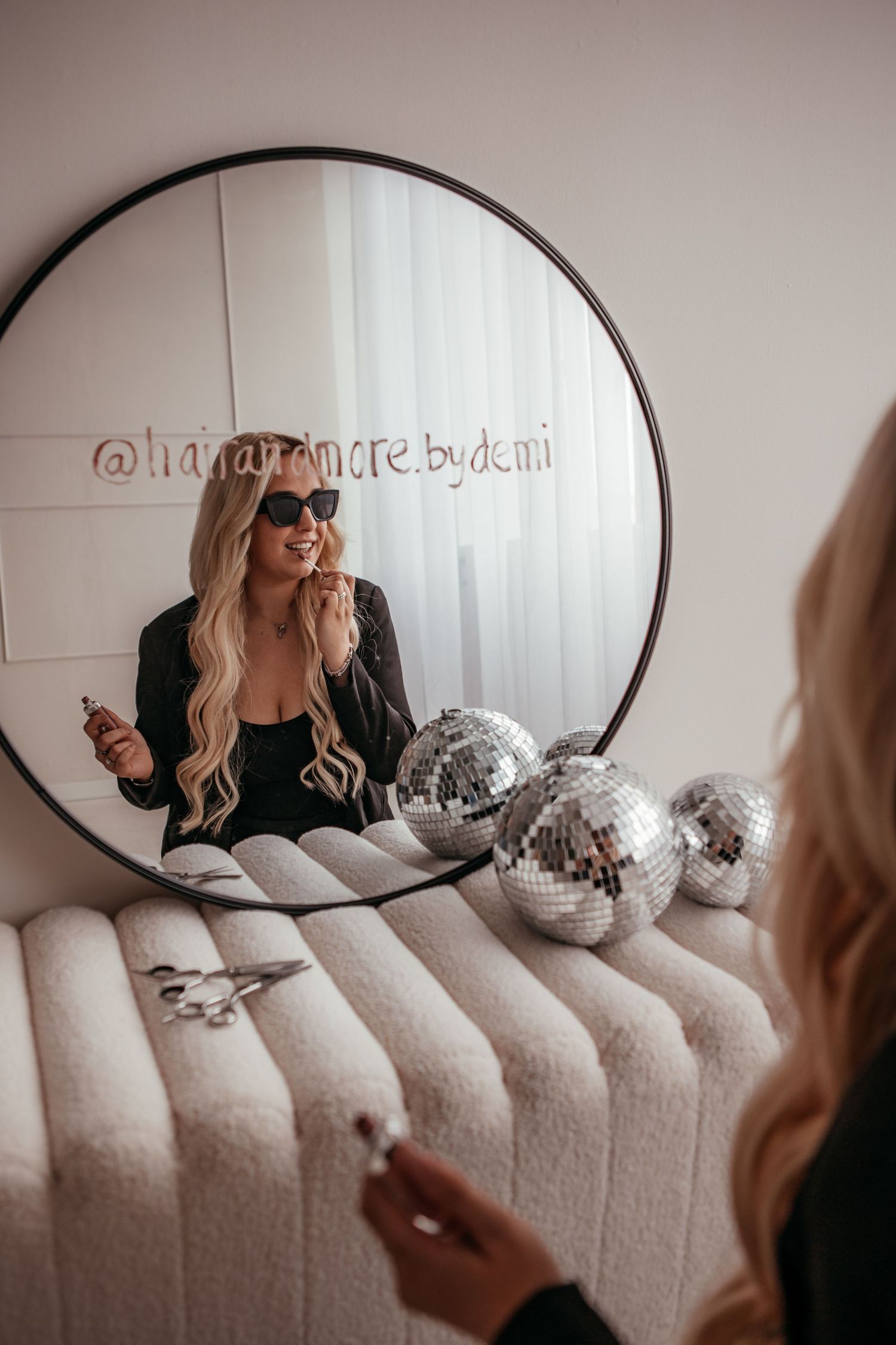 Blonde woman in sunglasses posing with a mirror reflection showing disco balls and her Instagram handle.