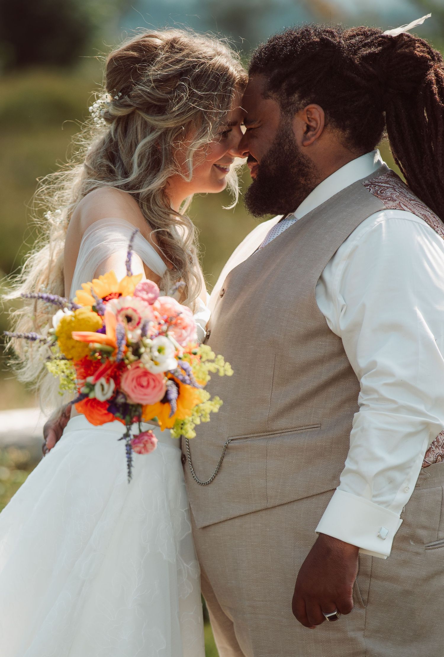 Interracial couple shares intimate moment holding colorful wedding bouquet outdoors.