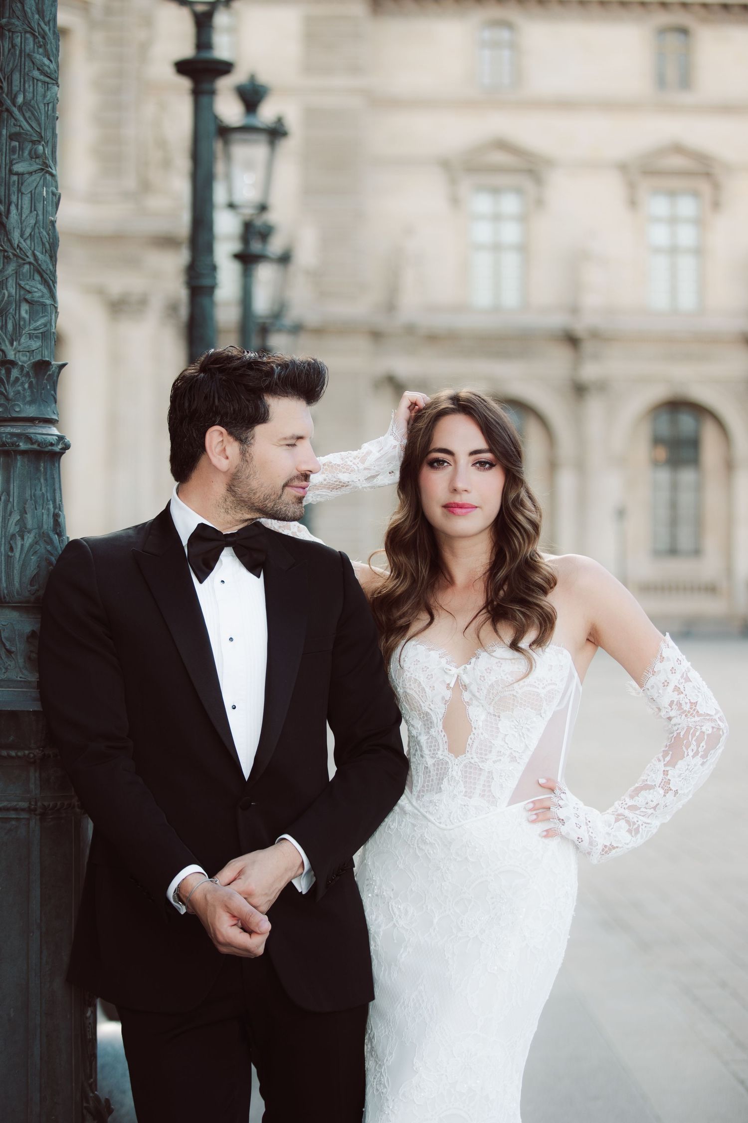 Bride in lace gown and groom in tuxedo pose by a vintage lamppost in Paris.