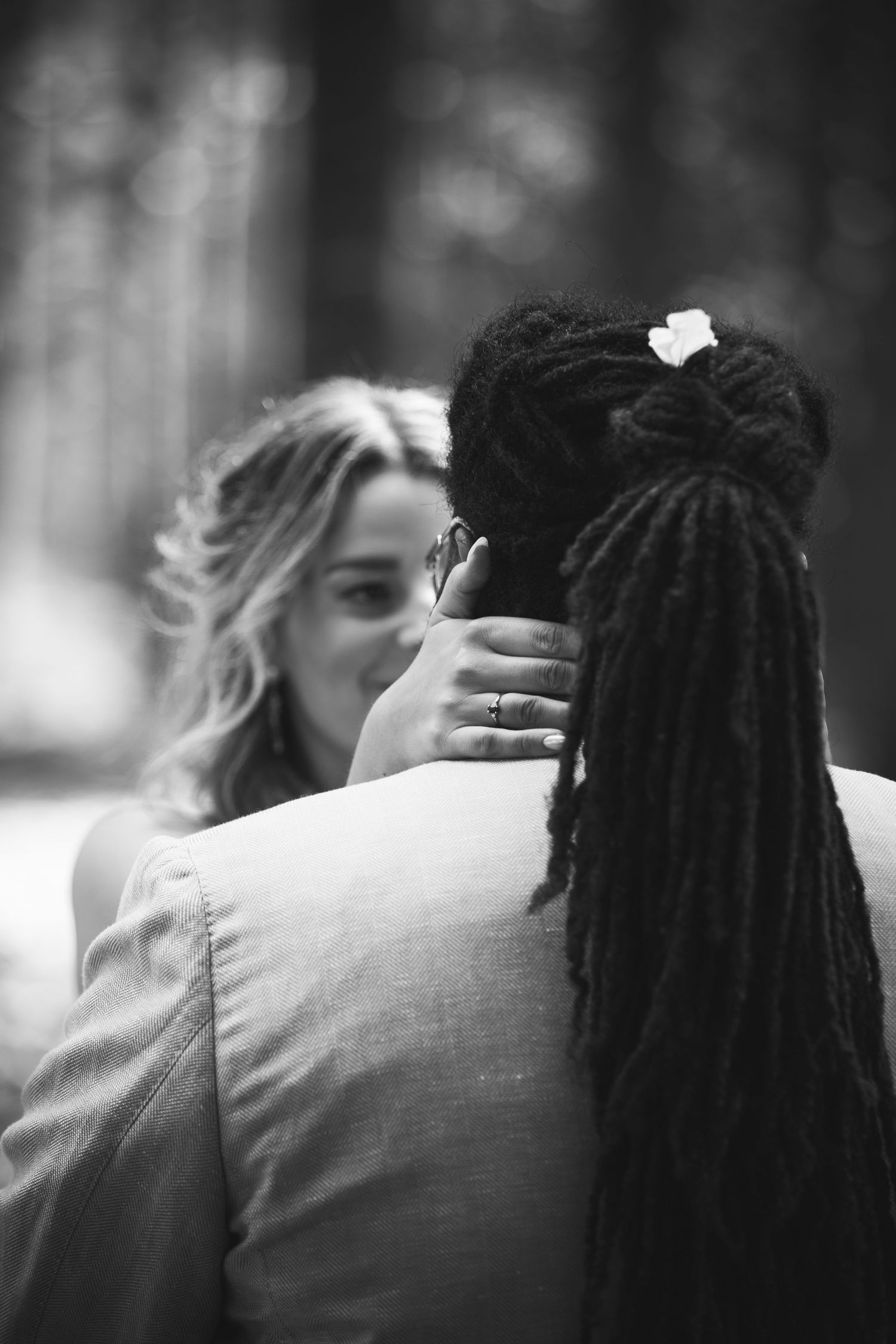 Black and white photo of bride embracing groom with dreadlocks at wedding.