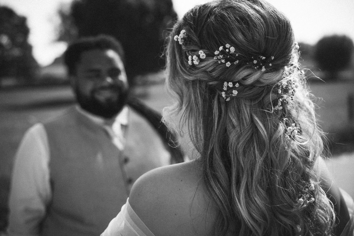 Black and white photo of a bride with floral hair accessories facing her groom outdoors.