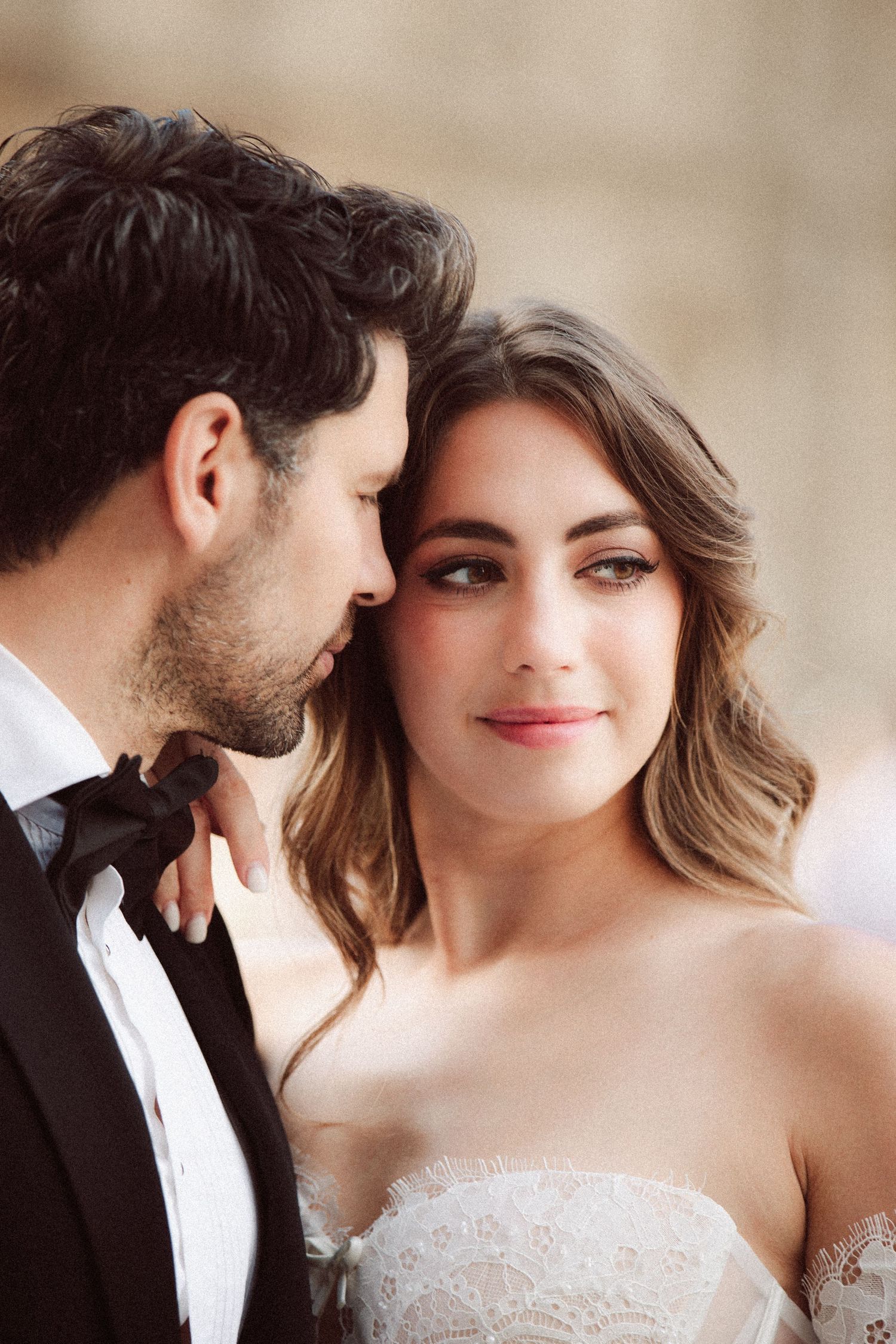 Close-up portrait of bride smiling softly beside groom in black bow tie tuxedo at outdoor Paris wedding.