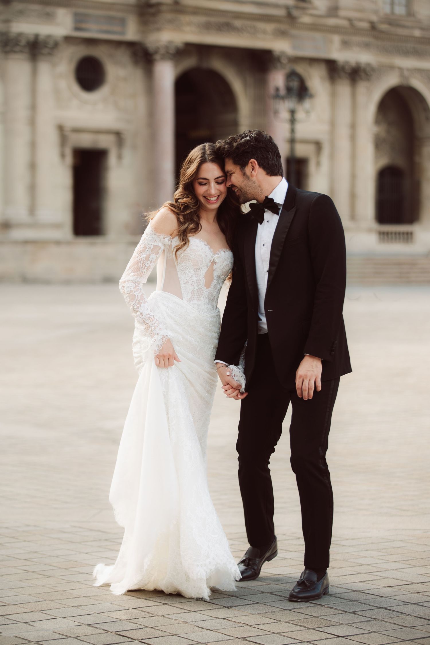 Smiling bride and groom walk hand in hand through a beautiful Parisian courtyard together.