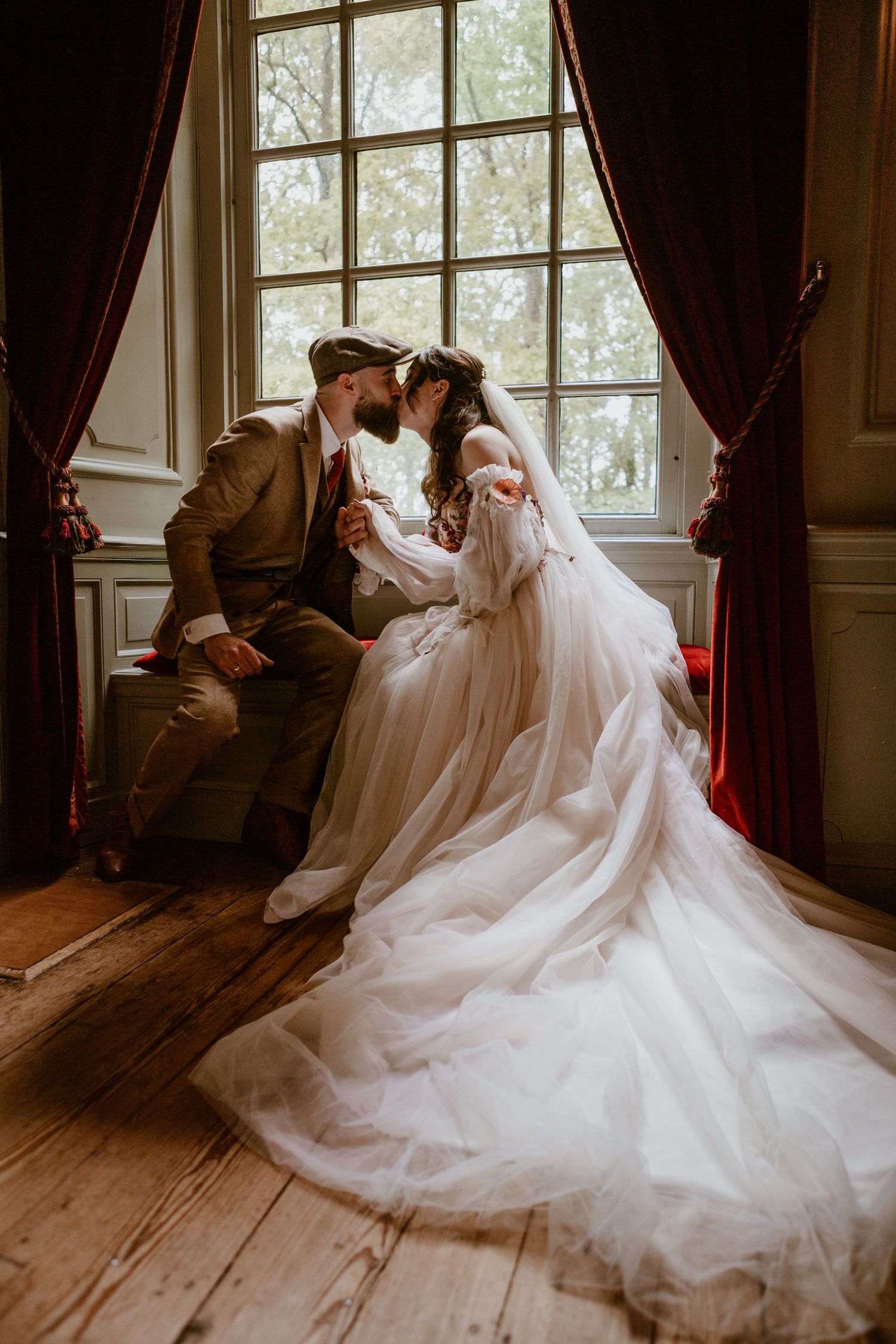 Bride and groom sharing an intimate moment seated by a large window in a rustic elegant venue.