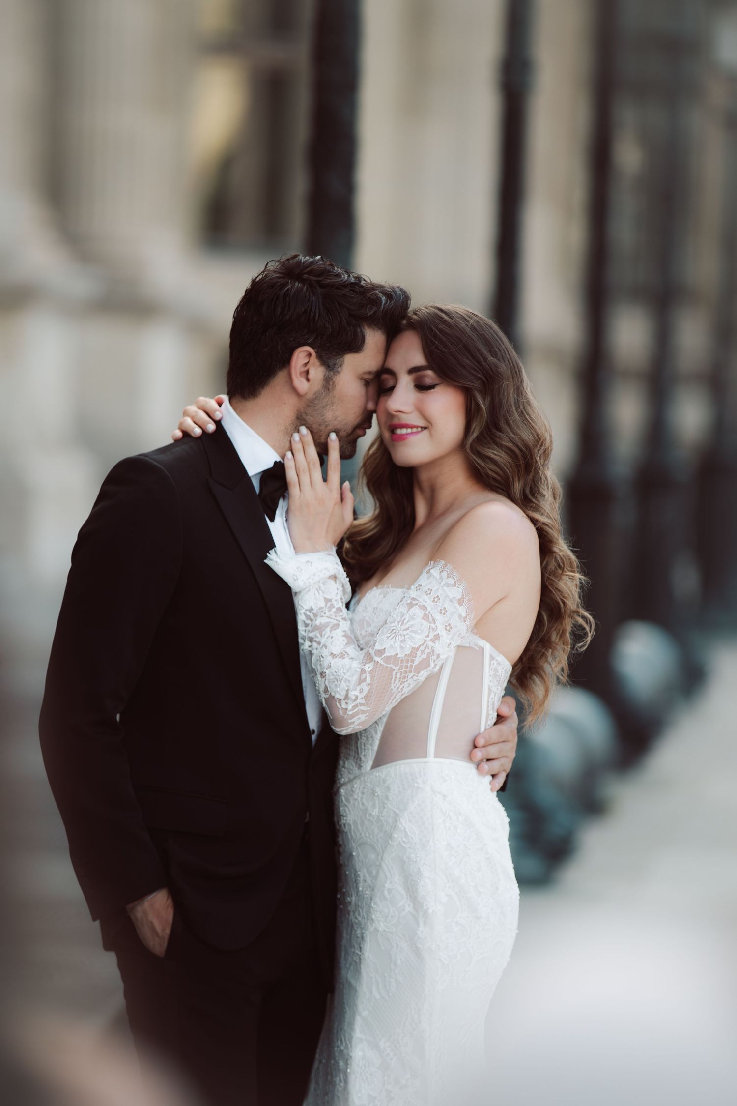 Romantic couple shares an intimate moment, bride in sheer lace wedding dress and groom in black tuxedo in Paris.