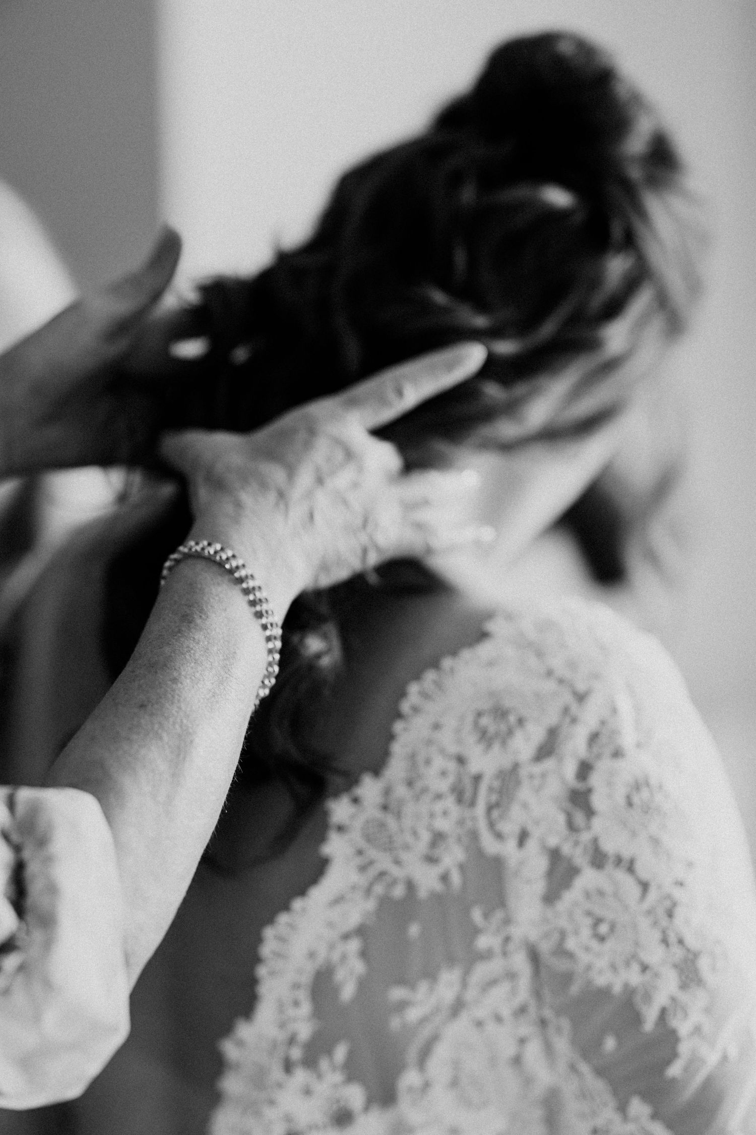 Black and white close-up of hands adjusting brides lace wedding dress and hair before ceremony.
