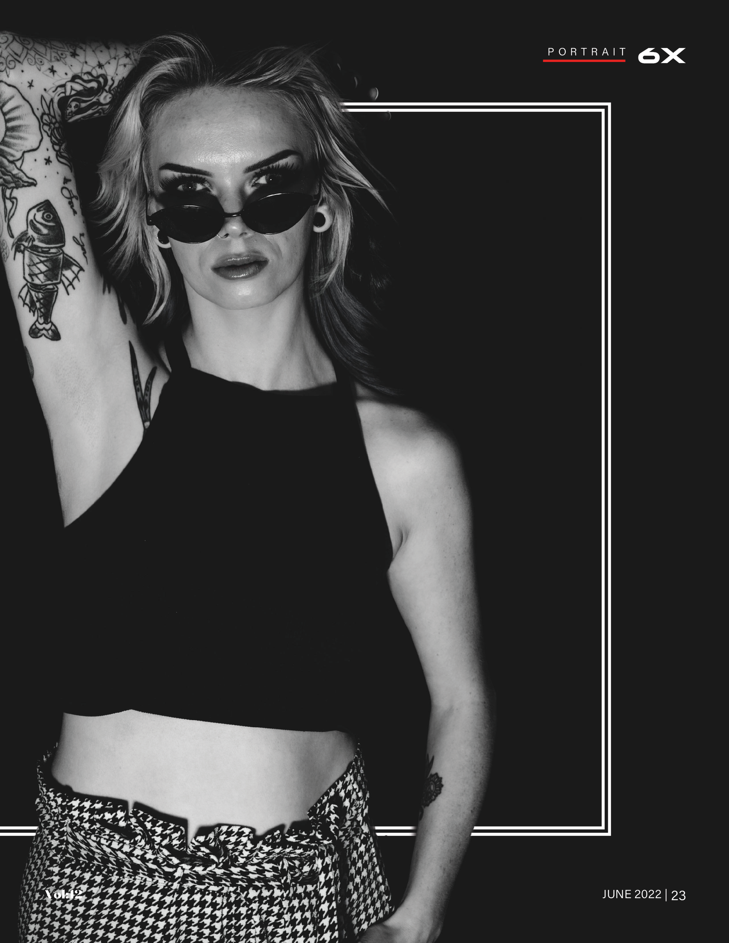 Black and white portrait of a blonde woman in sunglasses, crop top, and plaid skirt leaning against a wall.