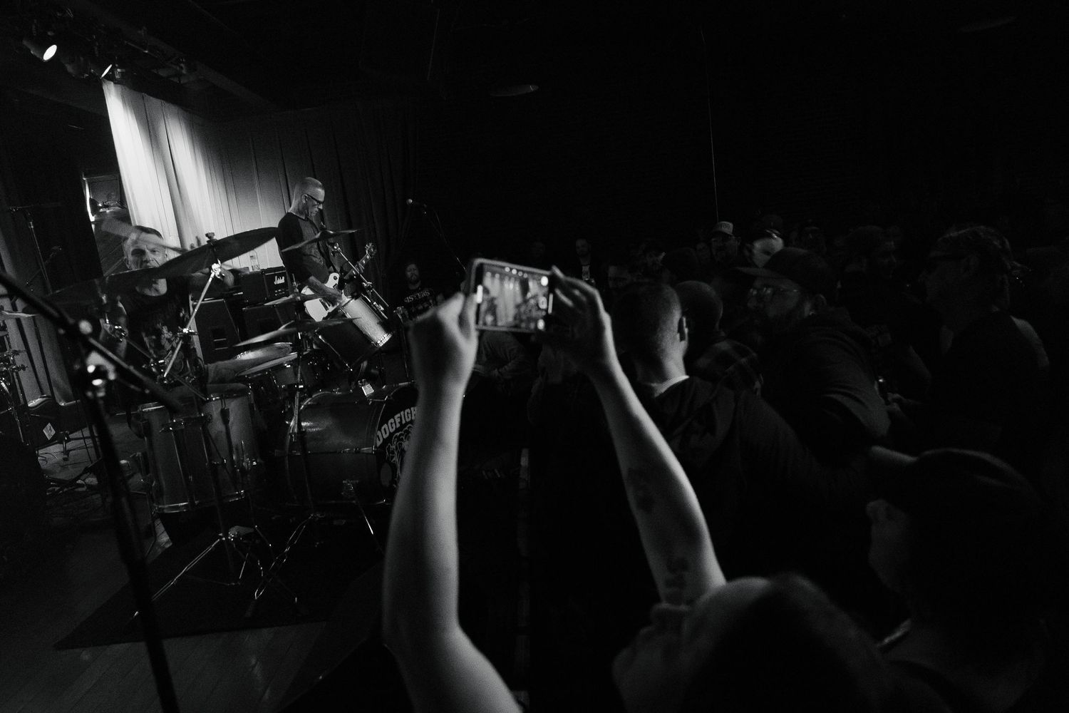 Concert crowd silhouettes with raised hands at a dark music venue.