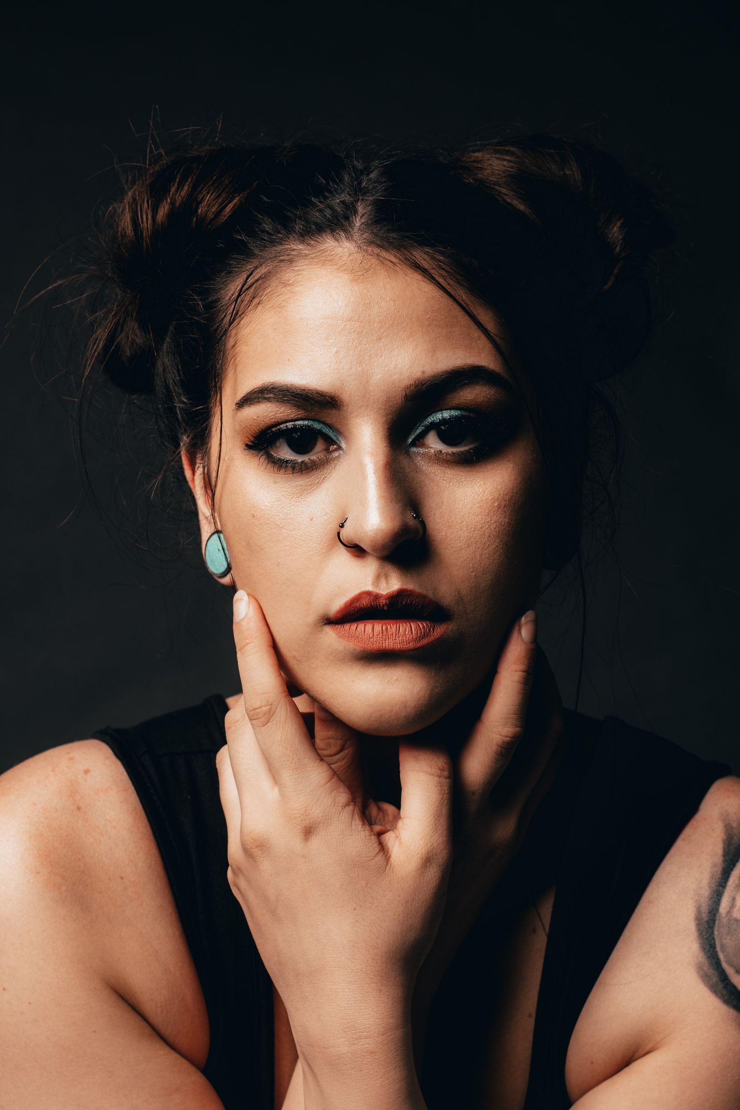 Studio portrait showing dramatic makeup and turquoise earrings against dark background.