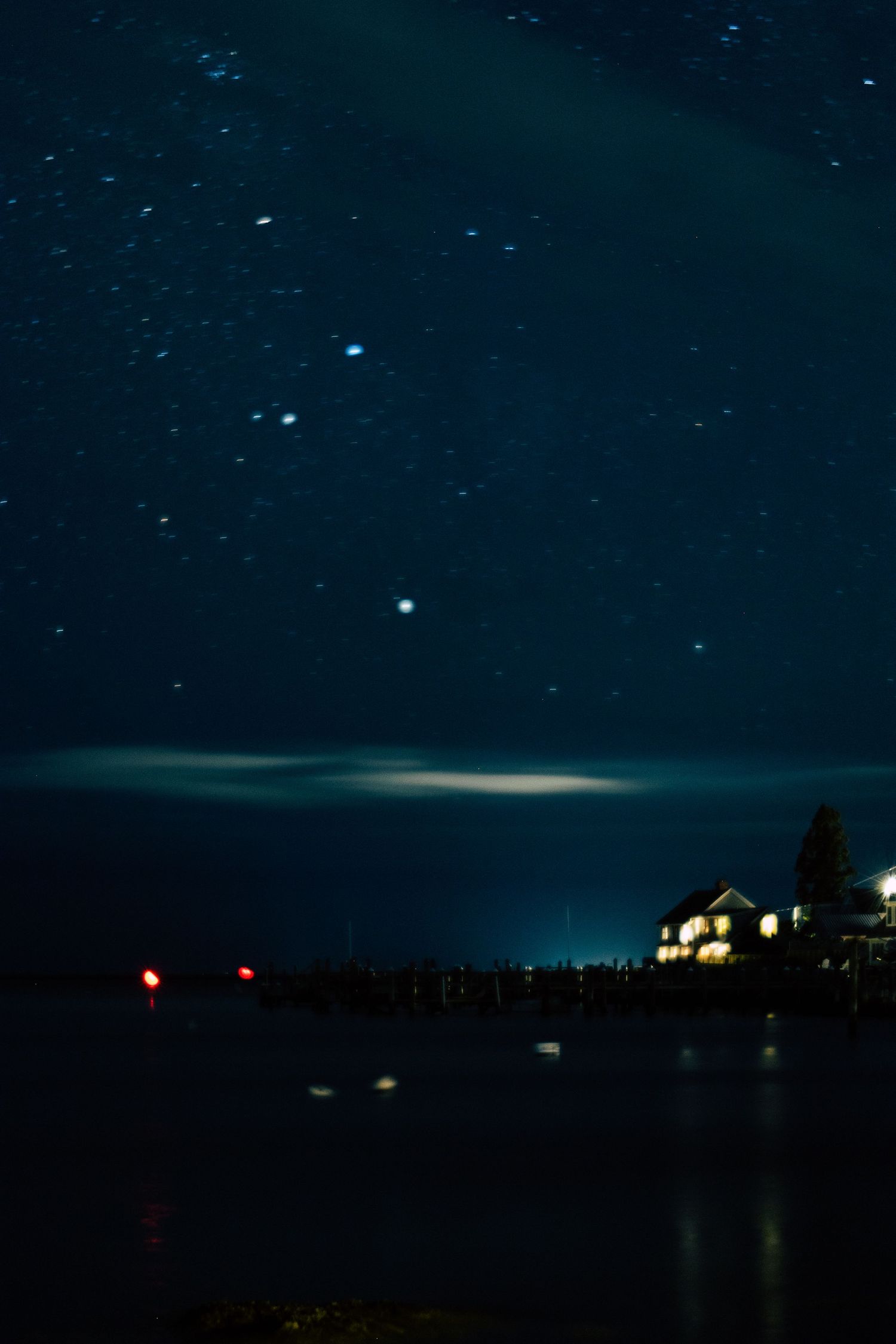 Starry night sky over a calm lake with a illuminated waterfront building reflecting lights on the water.