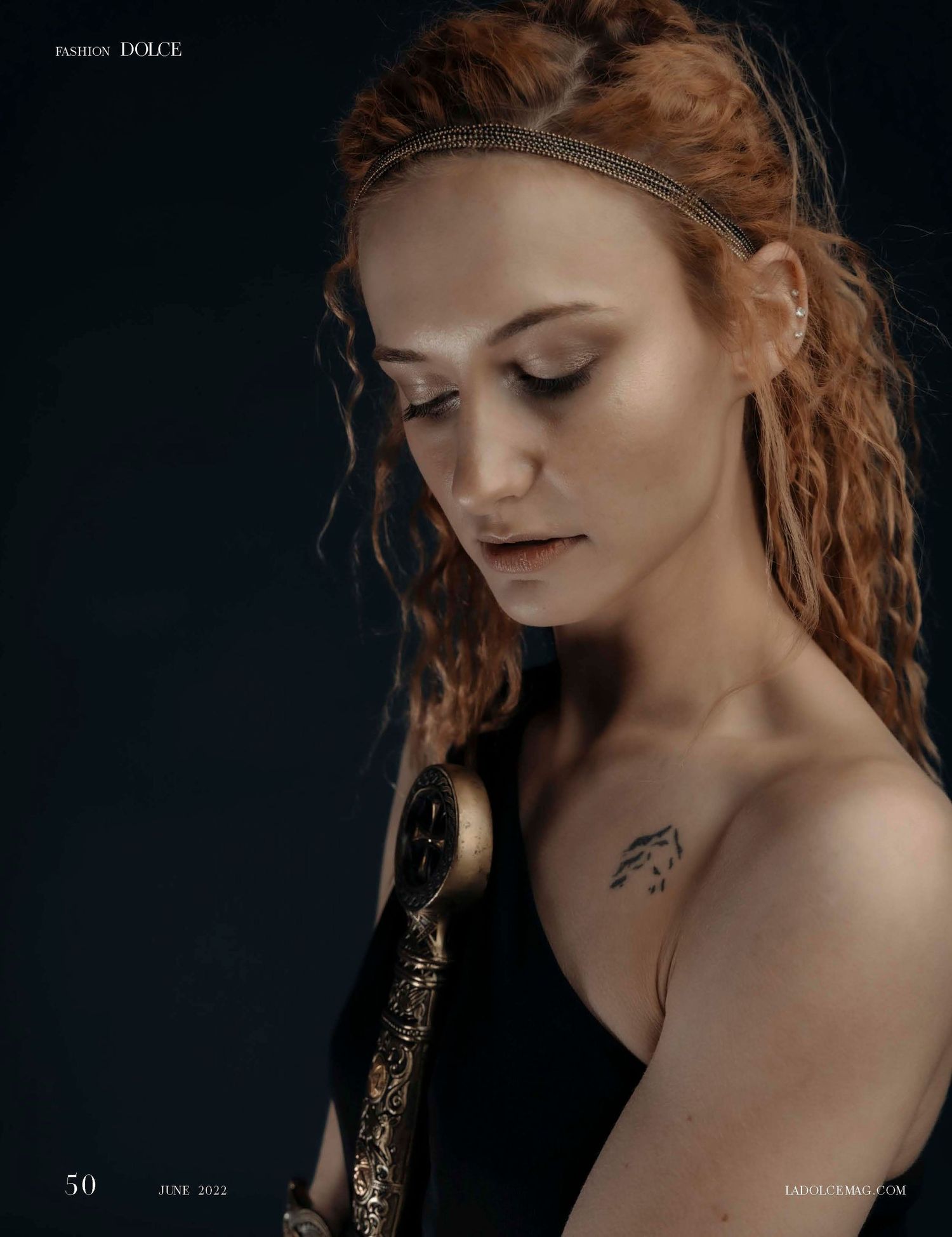 A red-haired woman holds a golden saxophone, wearing a black top with a small tattoo, featured in Dolce Fashion magazine.