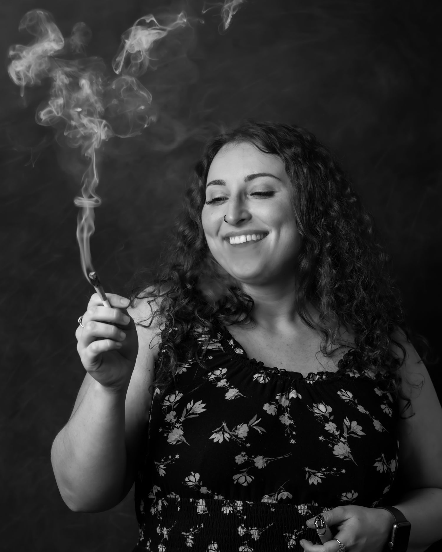 Black and white portrait of someone in floral dress smiling while smoking.