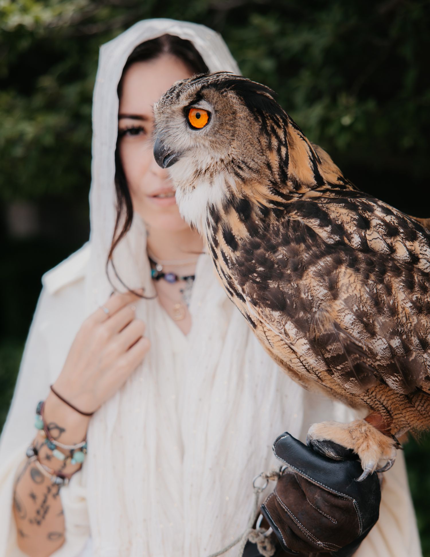 White-cloaked figure with owl in artistic outdoor photoshoot.