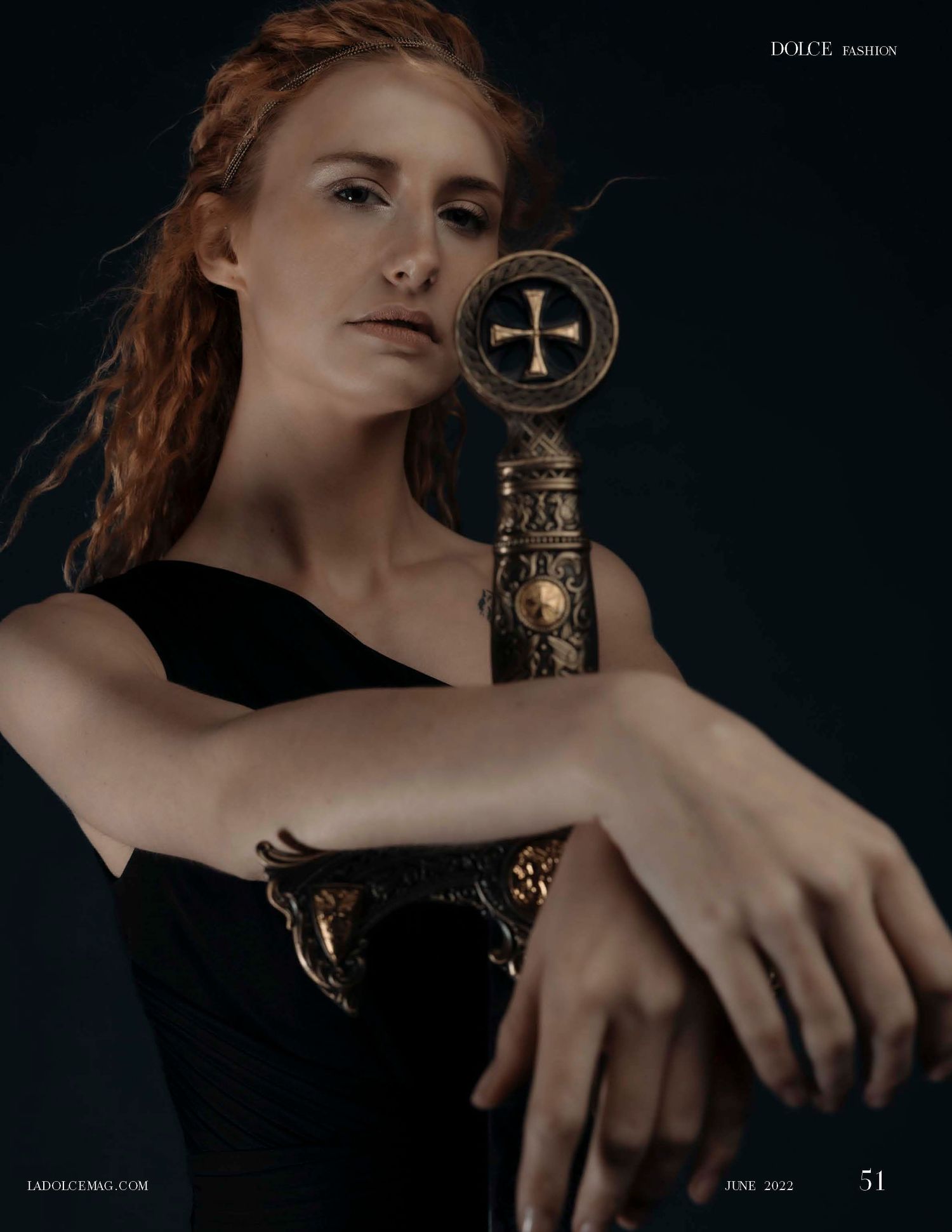 Red-haired woman in black dress holding ornate sword with cross pommel, Dolce Fashion magazine June 2022.