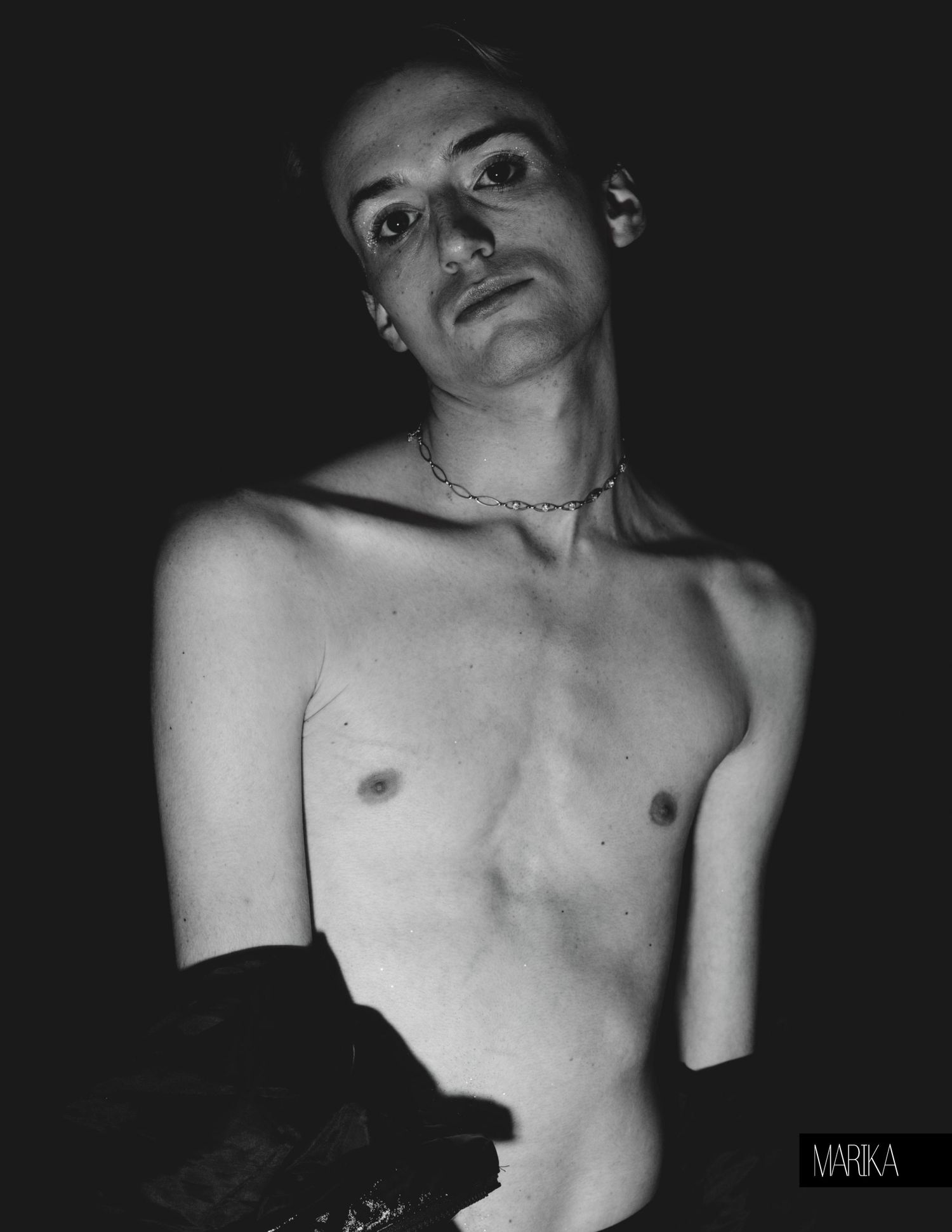 Black and white portrait of a shirtless person wearing a chain necklace, looking upward dramatically.
