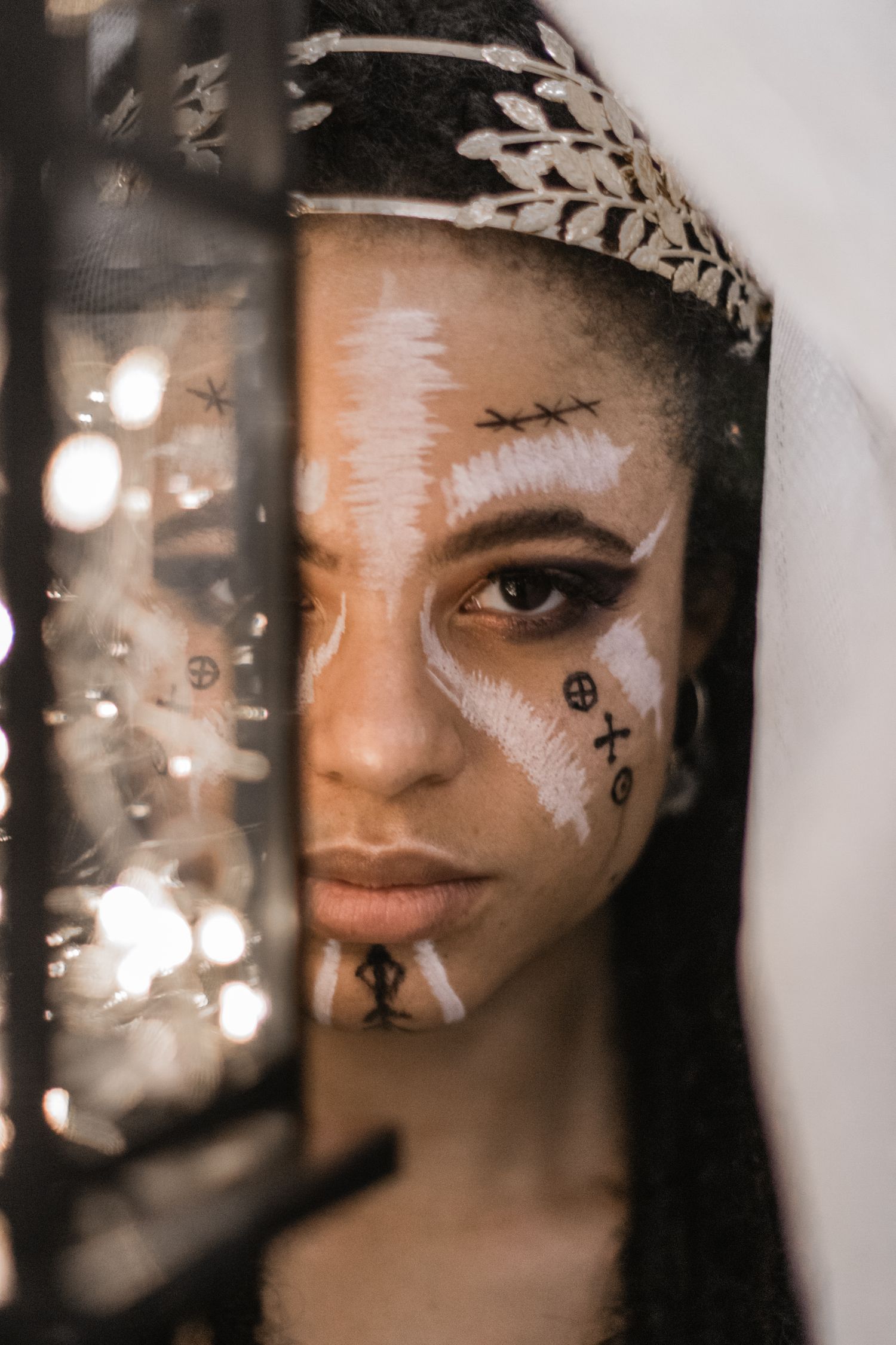 Creative portrait with delicate face paint and silver headpiece in soft lighting.