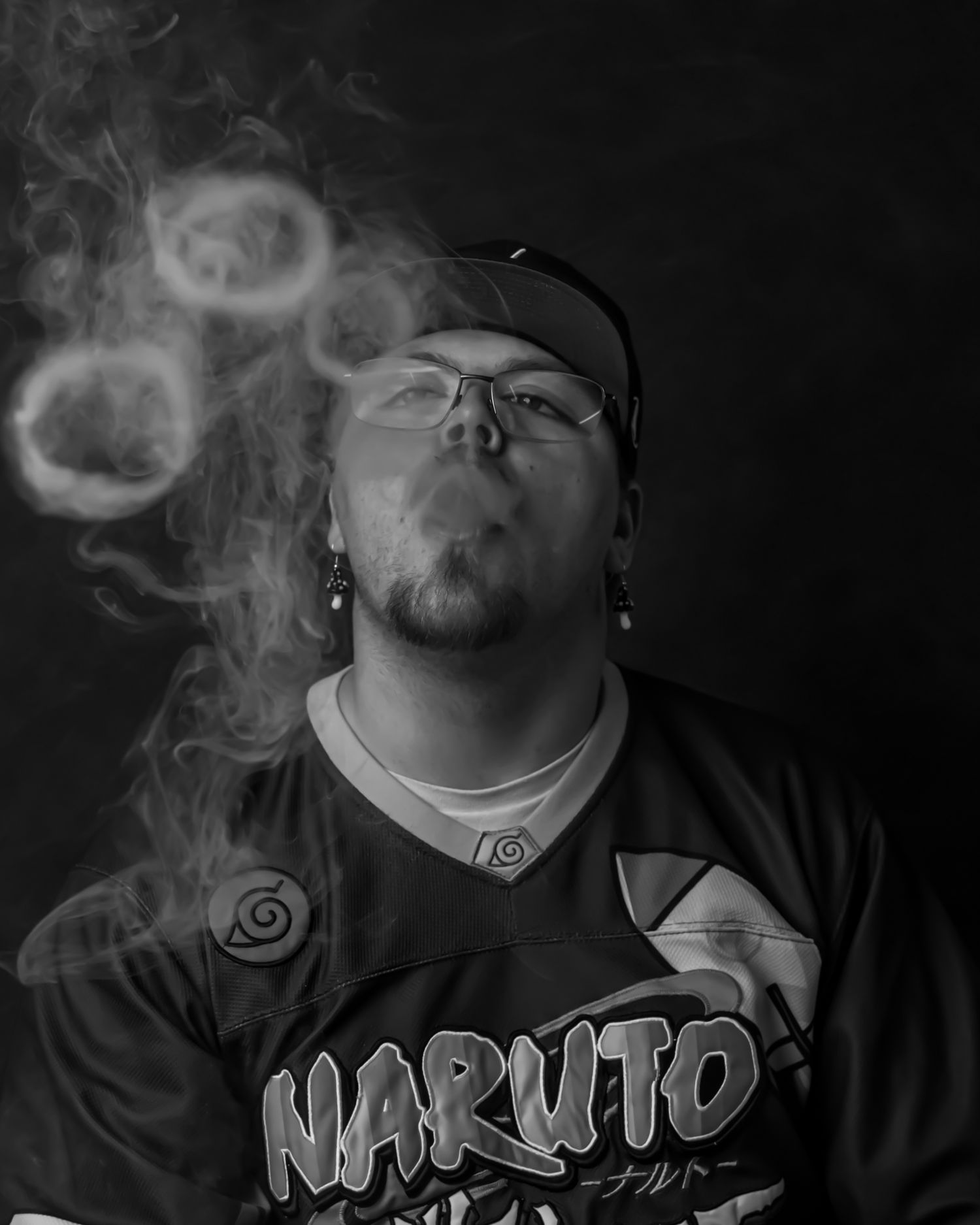 Black and white photo of someone in Naruto shirt blowing smoke rings.