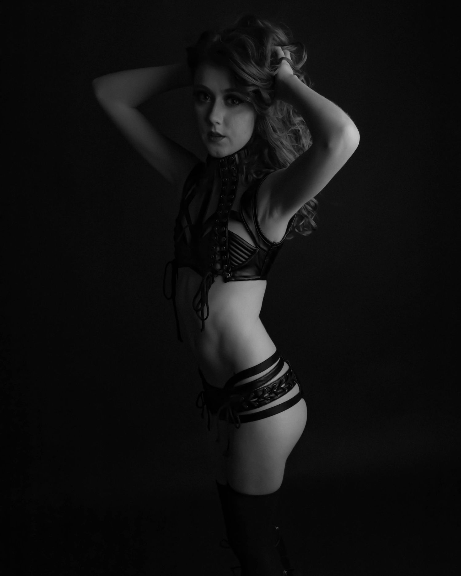 Black and white artistic portrait of a woman in dark lingerie posing against a dark studio background.