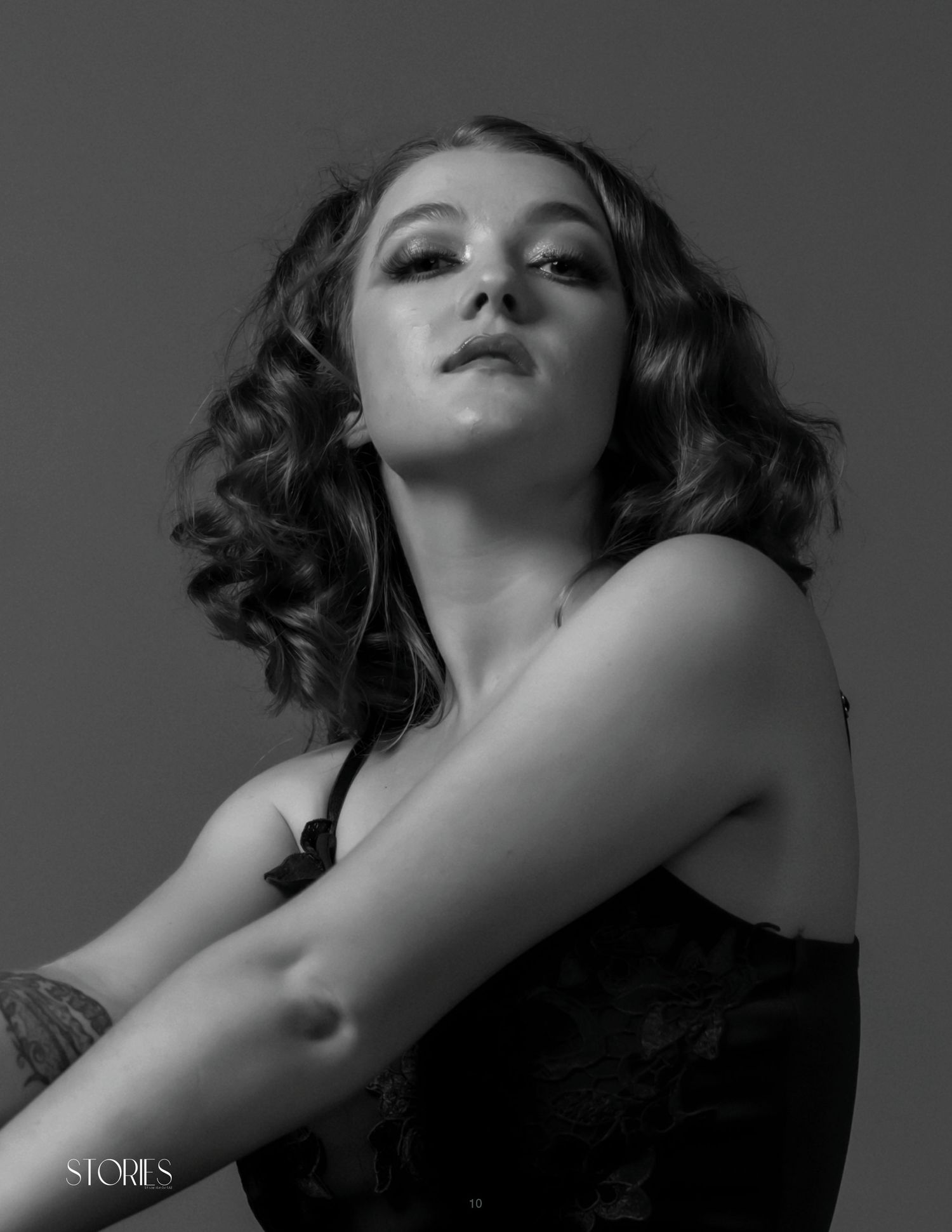 Black and white portrait of a young woman with curly hair in a dark top, gazing upward in a dramatic pose.