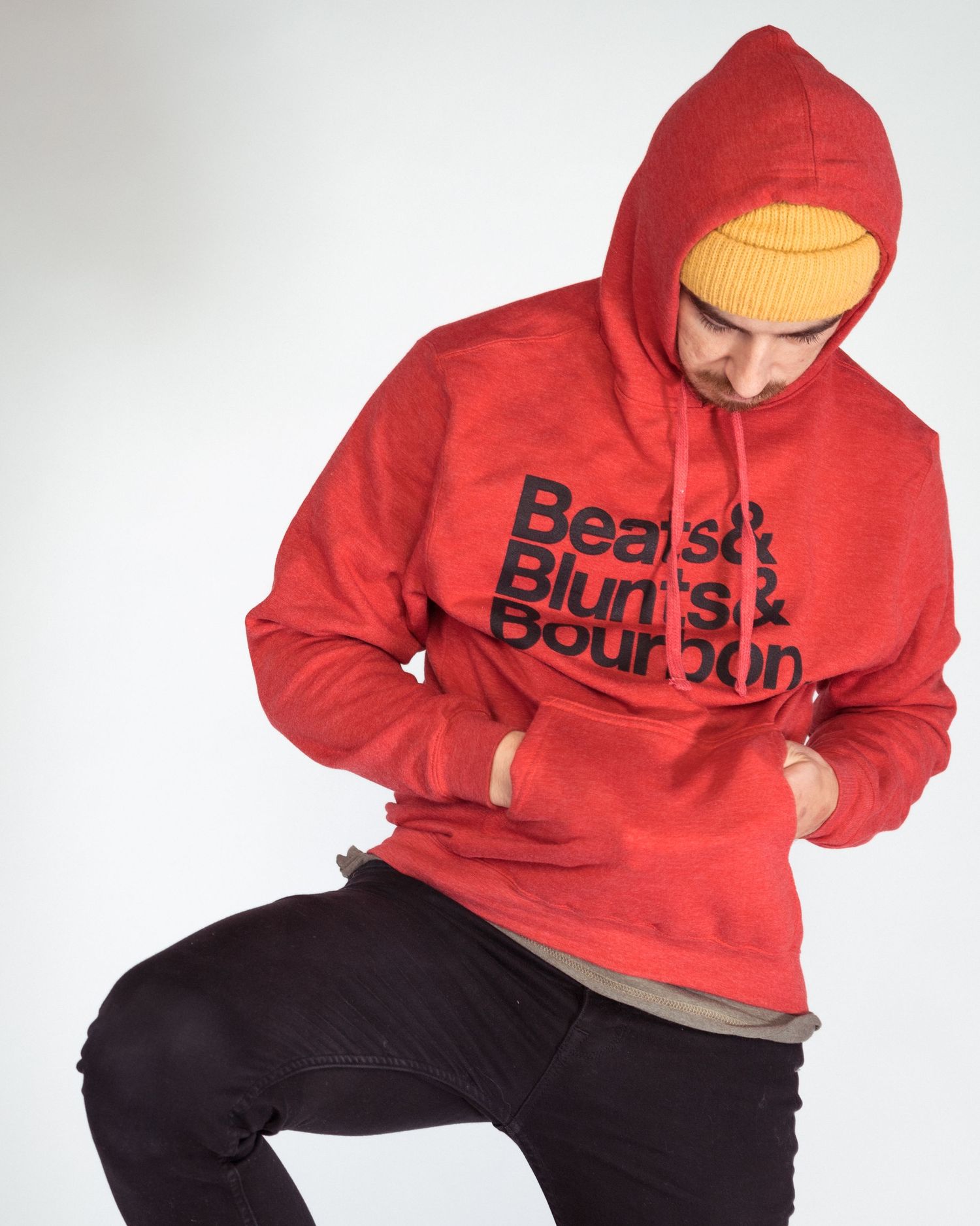 Man wearing red hoodie with Beards, Blunts & Bourbon print and yellow beanie, posing against white background.