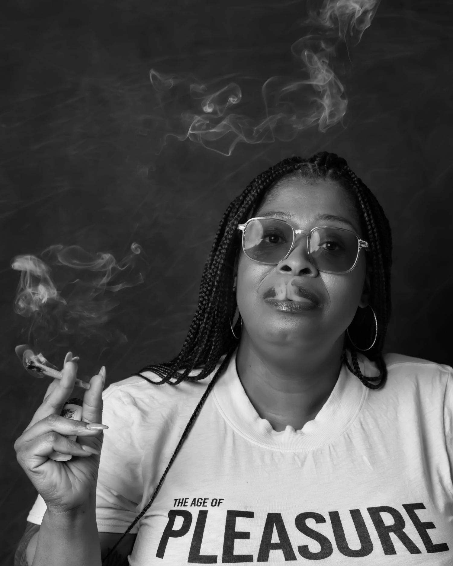 Portrait of someone wearing a Pleasure t-shirt and glasses exhaling smoke.
