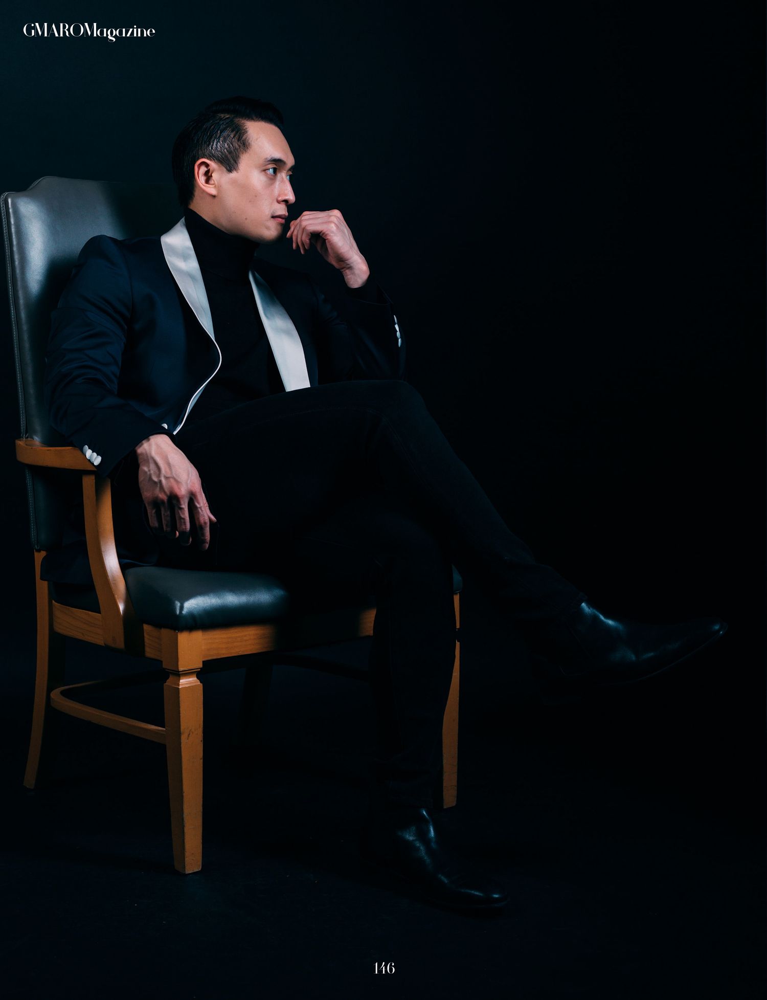 Moody portrait of person in suit sitting thoughtfully in wooden chair against dark backdrop.