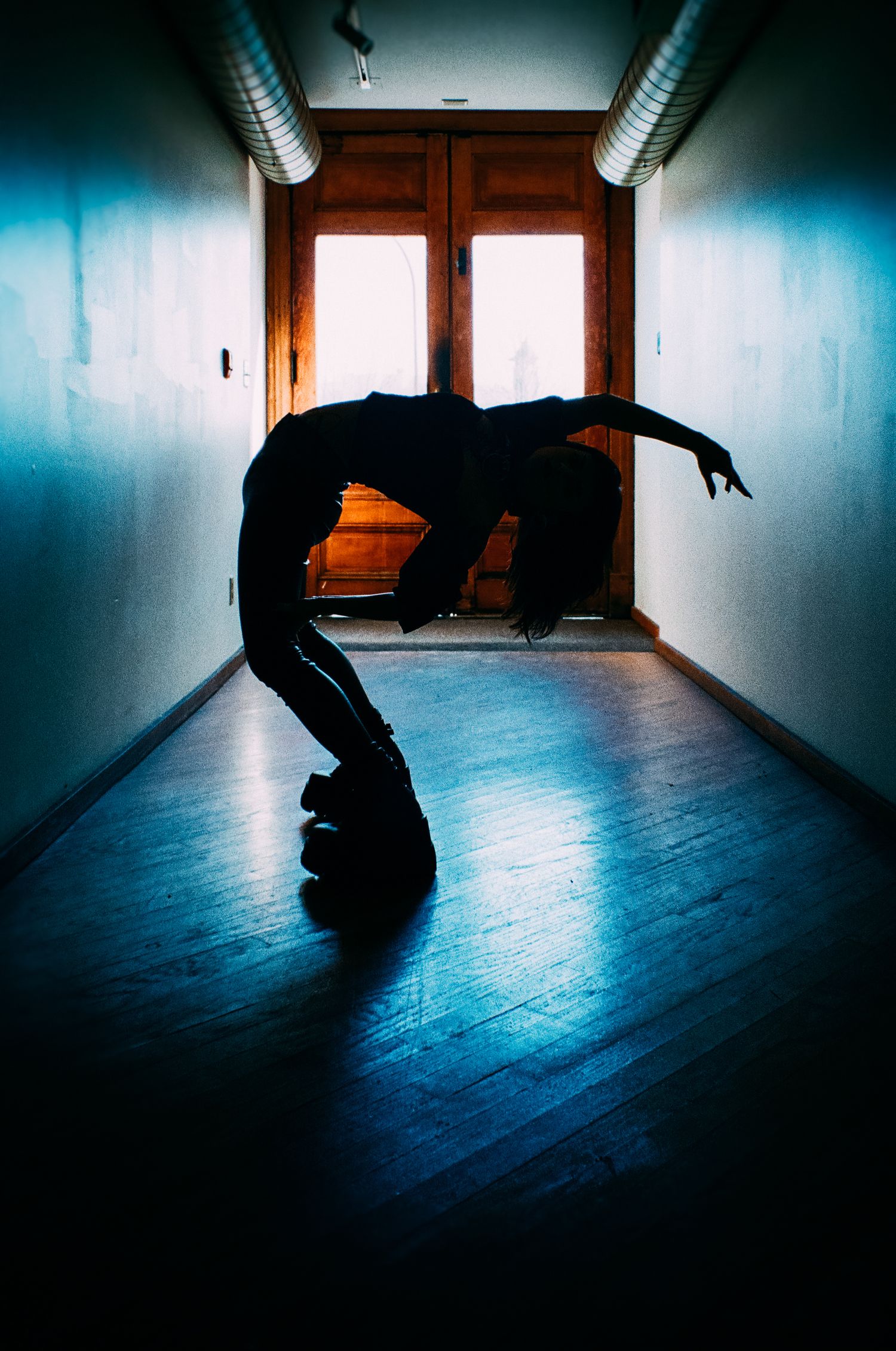 Silhouetted figure performing an artistic backbend in a dimly lit hallway with dramatic lighting.