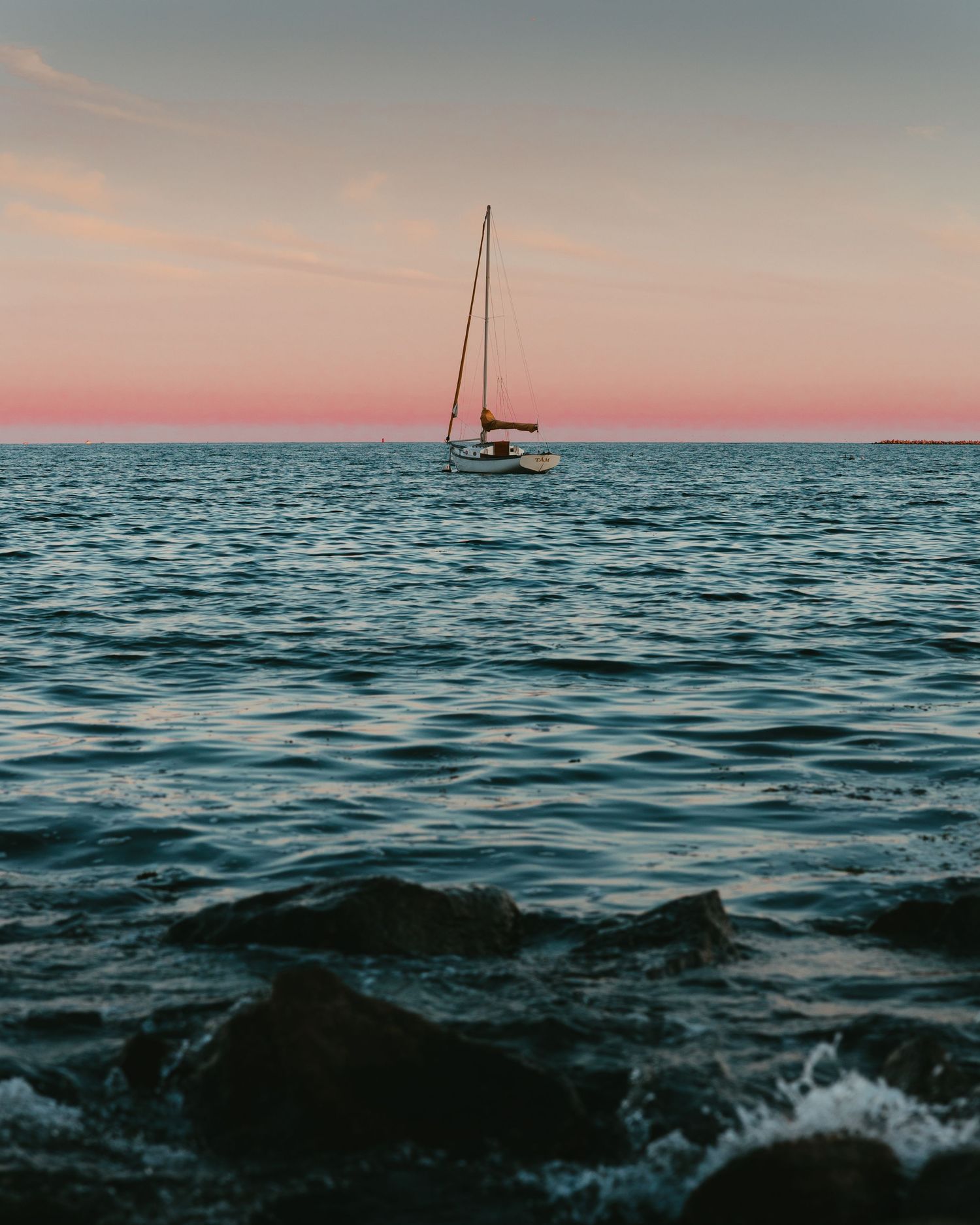 Sailboats silhouetted against a pastel sunset on calm ocean waters.