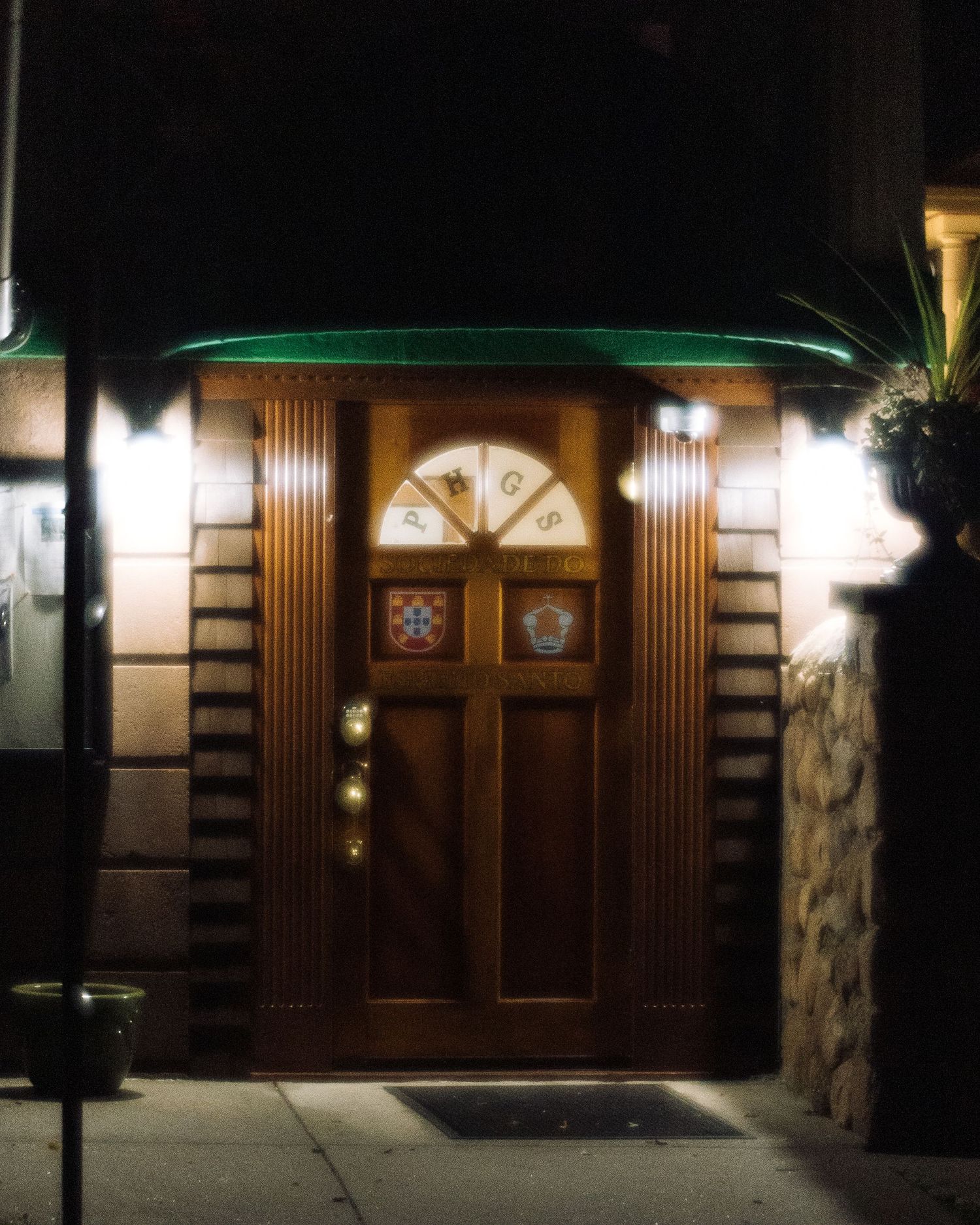 Ornate wooden door with stained glass fanlight and decorative crests, illuminated at night by warm lights.