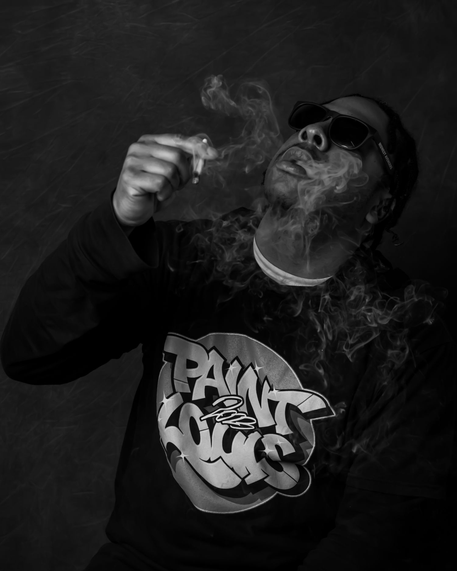 Black and white portrait of someone wearing a Phat Nuts shirt exhaling smoke.