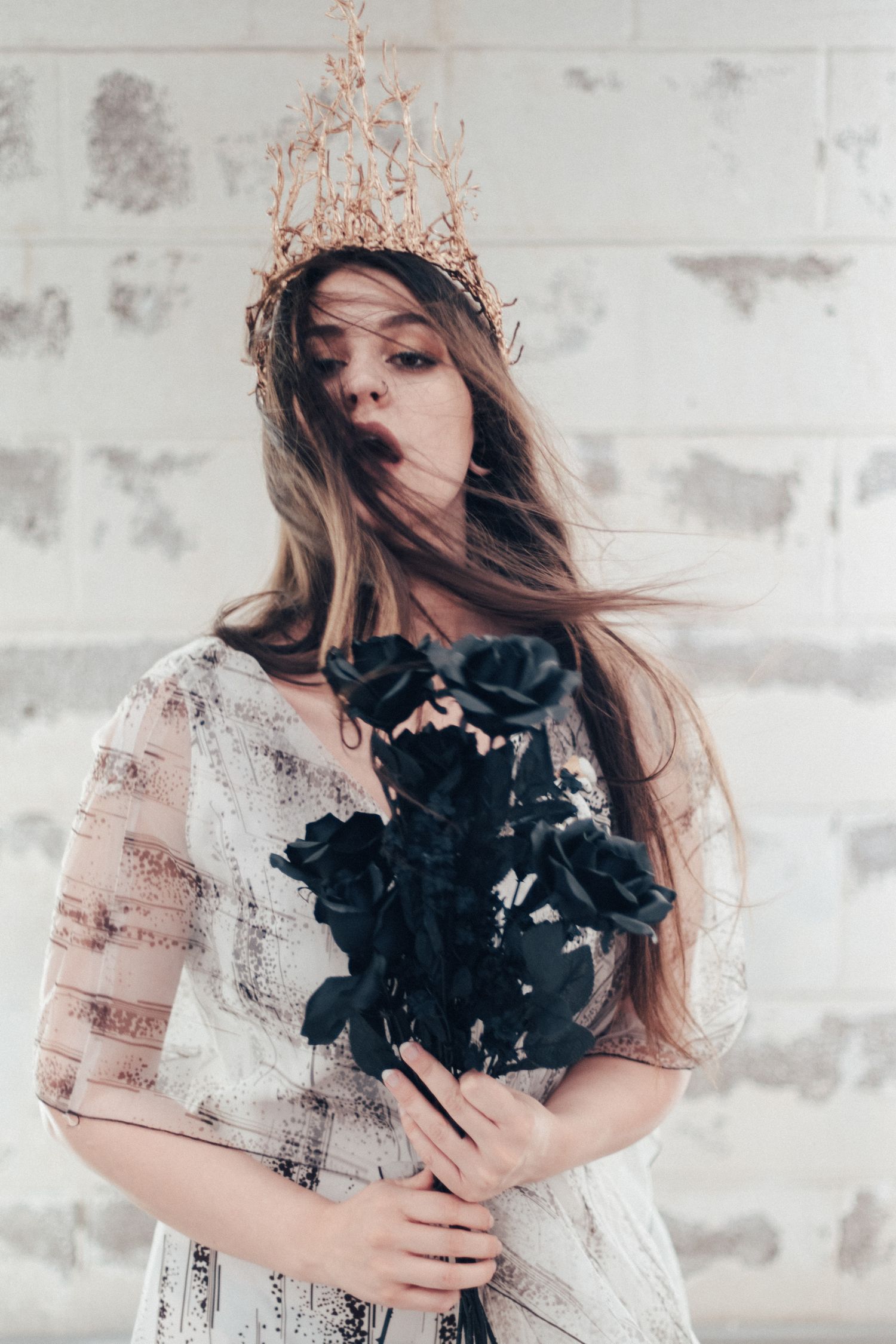 Ethereal portrait with copper crown, flowing hair, and black flowers against textured wall.