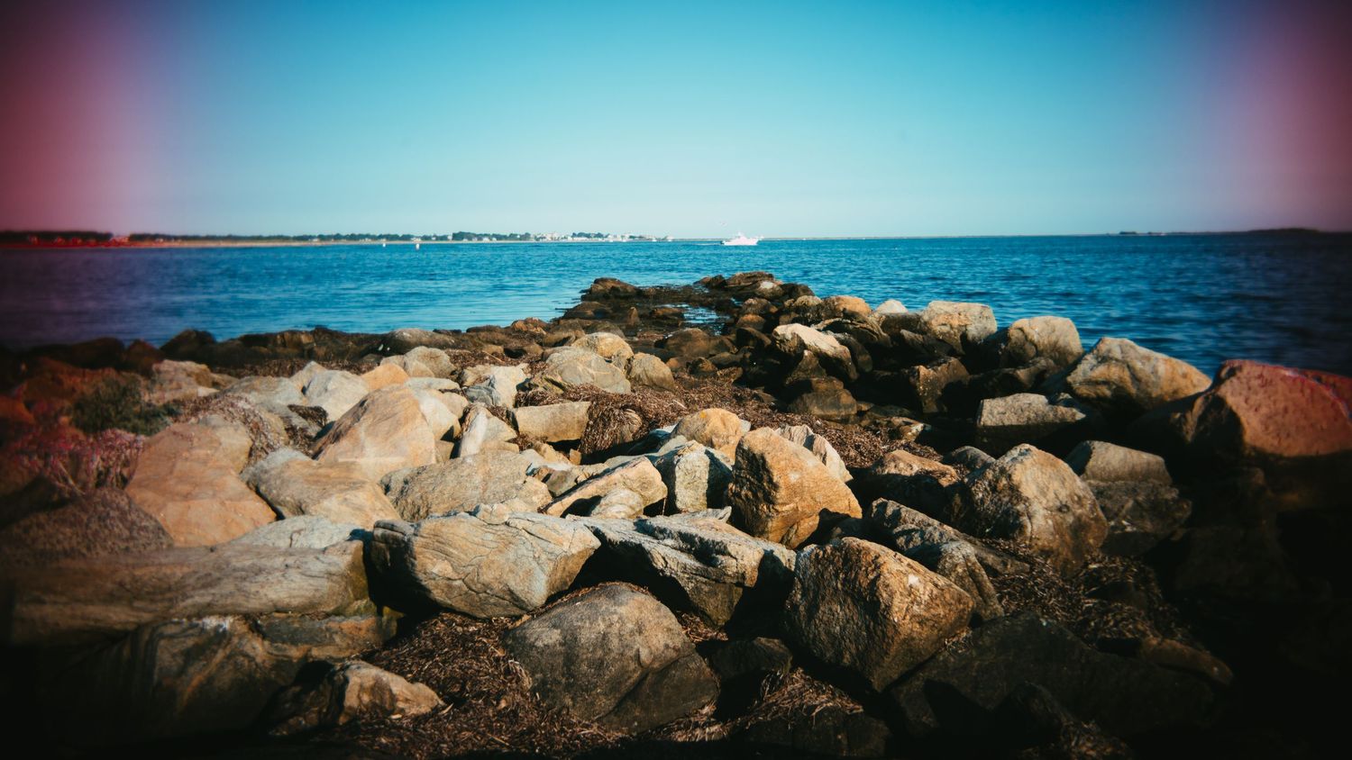 Rocky coastline panorama with blue ocean and pink-tinted sky.