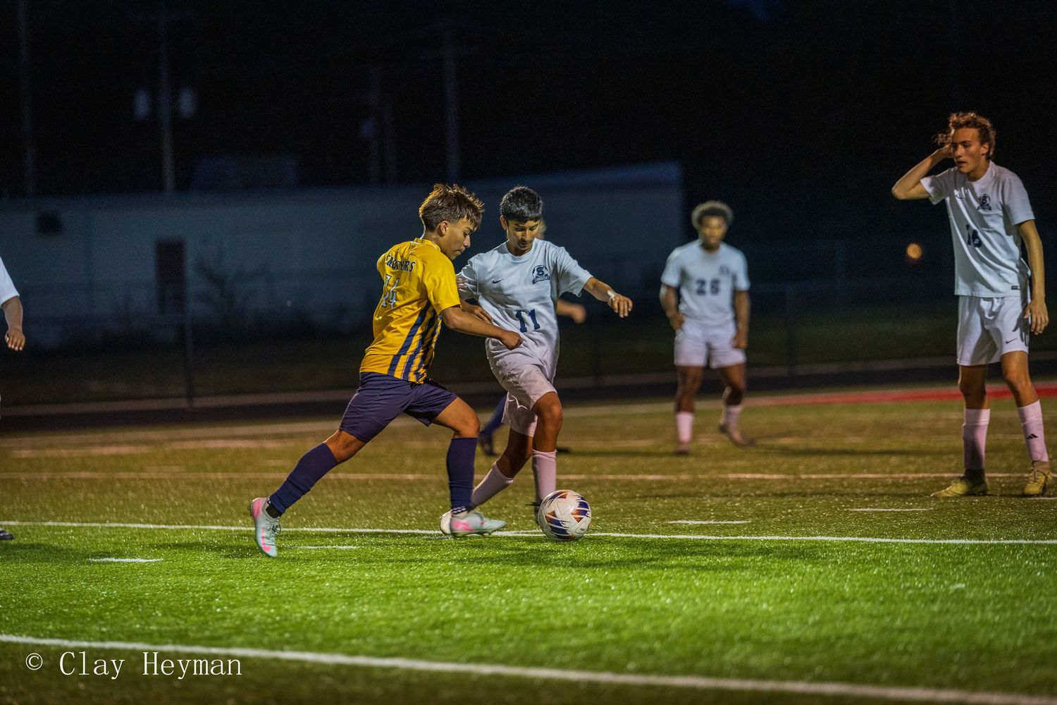 Soccer players competing for ball during nighttime match on lit field.