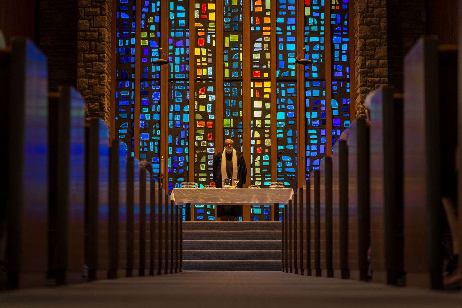 Stunning stained glass windows illuminate church altar with colorful light during religious ceremony.
