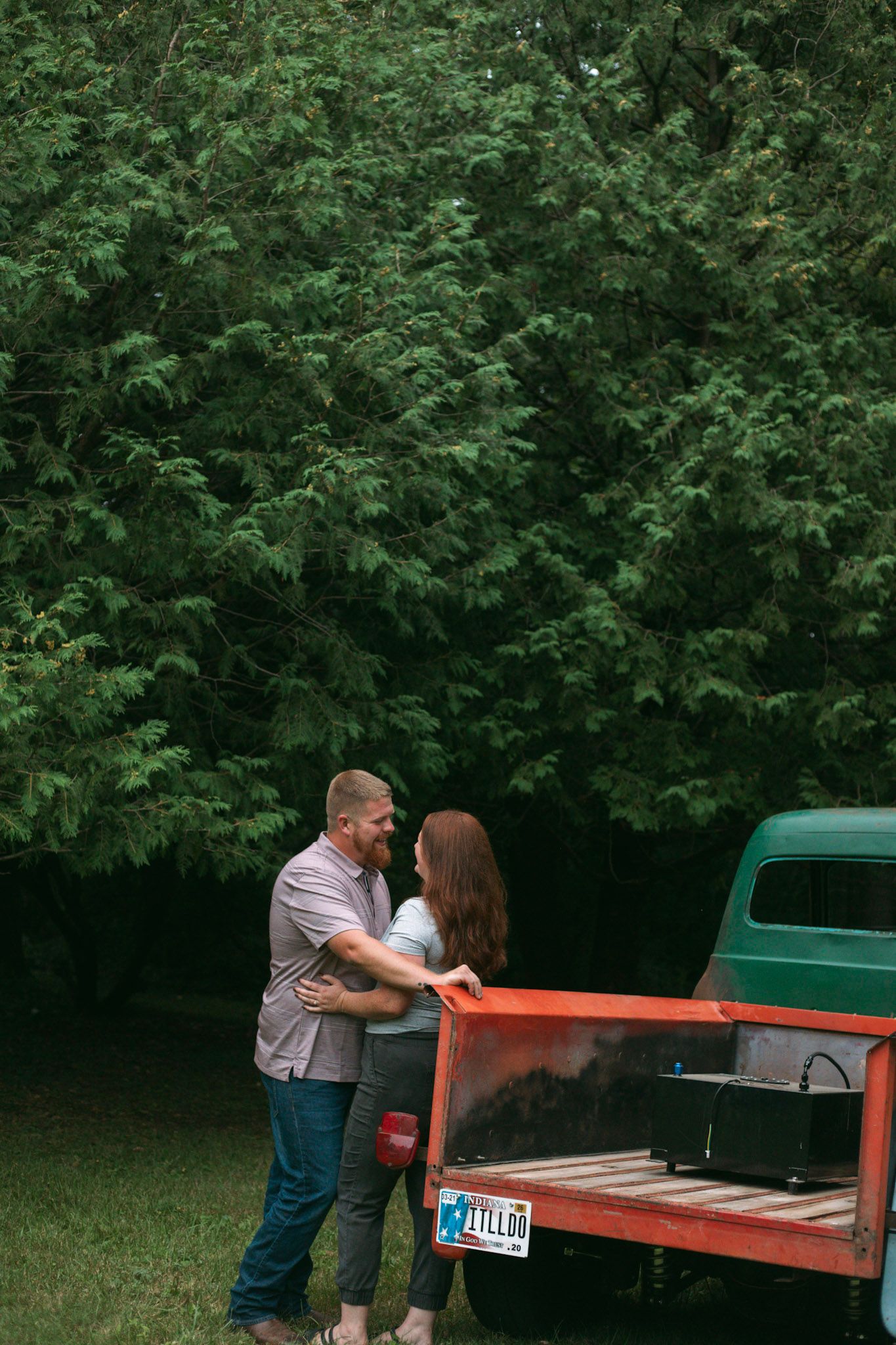Couple embracing and smiling at each other beside a vintage red and green truck outdoors.