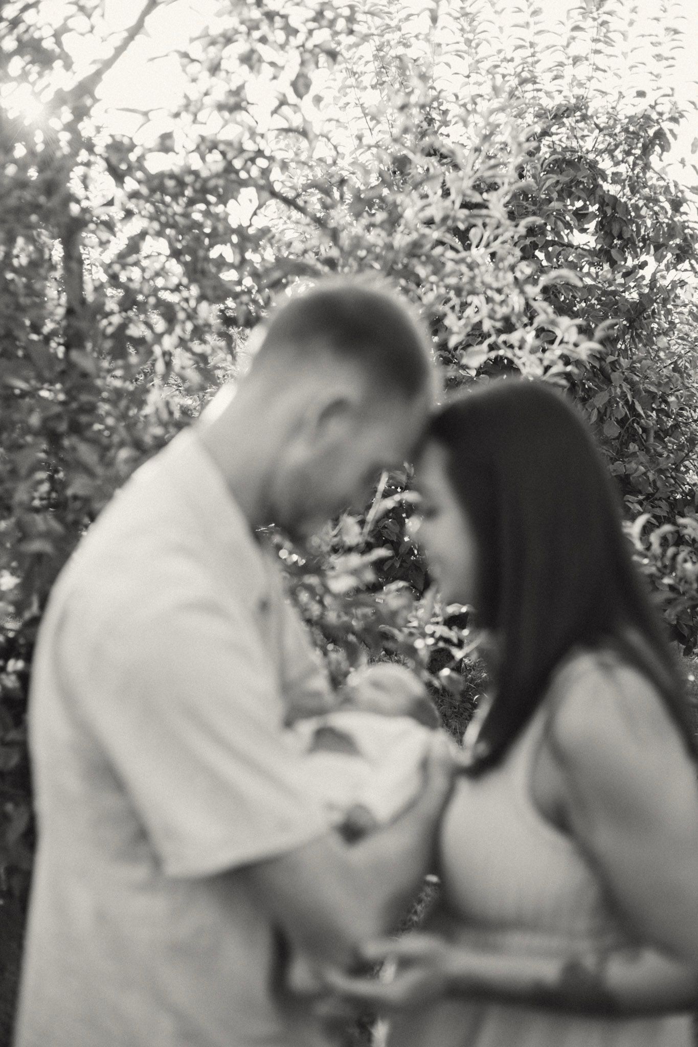 Blurred black and white photo of a couple cradling a newborn in a garden.